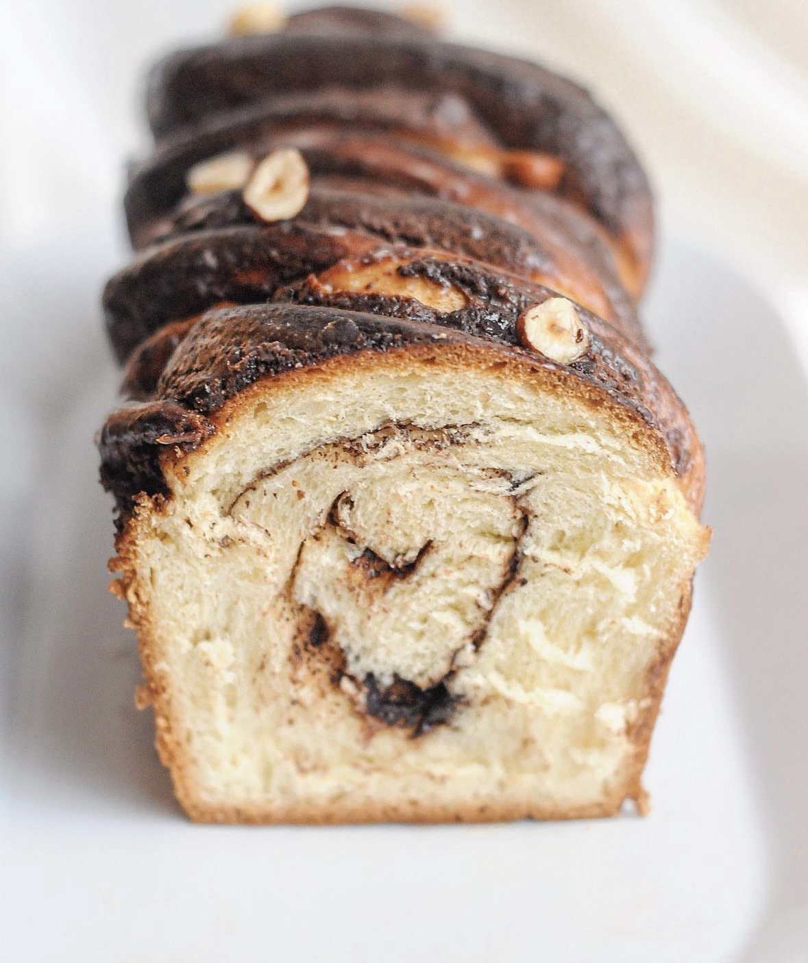 Babka au chocolat, décoré de noisettes sur le dessus, posé sur une surface blanche.