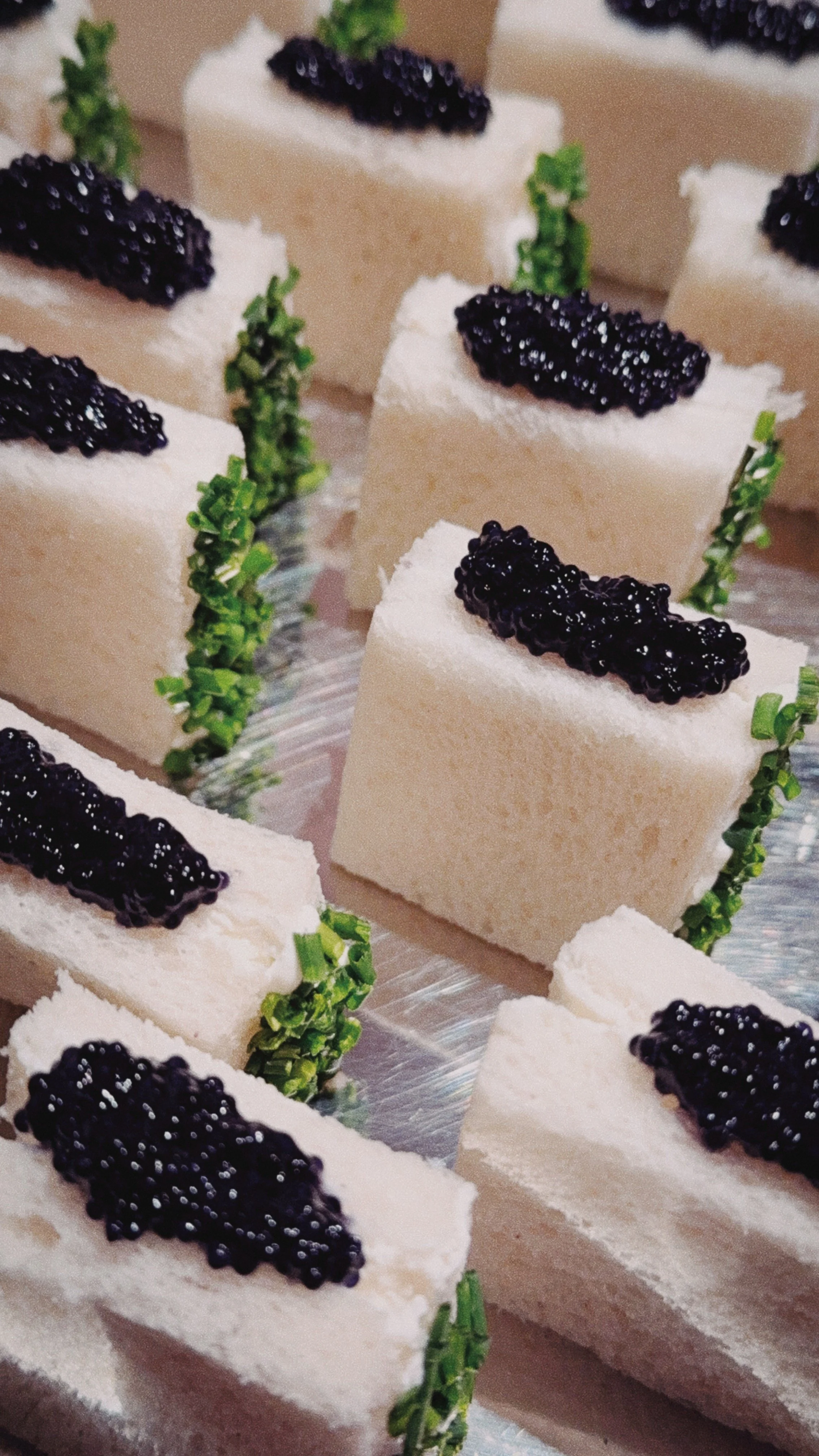Petits sandwiches à base de pain blanc, garnis de caviar noir et décorés avec des brins de ciboulette.