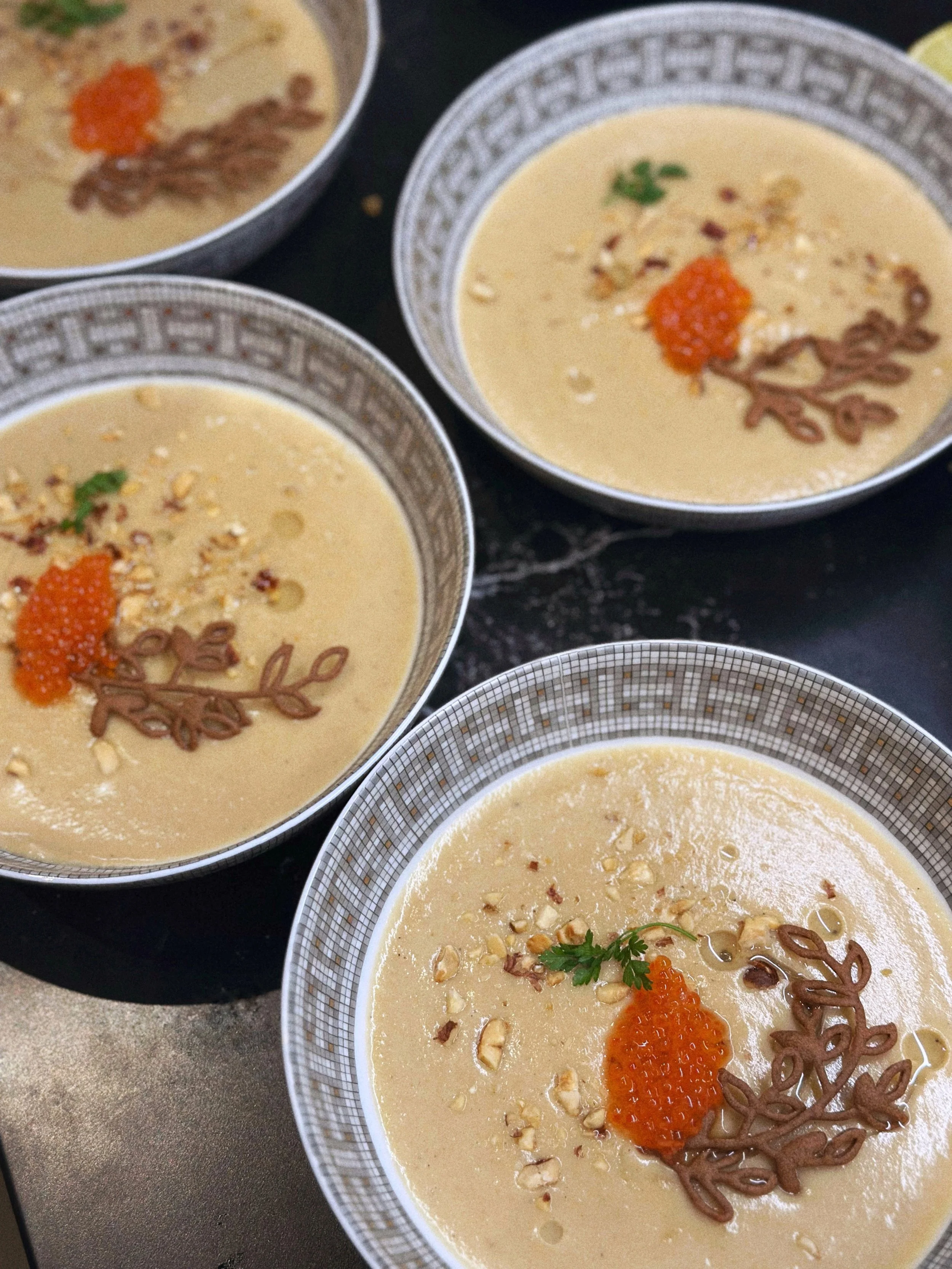 Crème de topinambour avec tuile de sarrasin, oeufs de truite et herbes, servie dans un bol hermès avec un motif géométrique.