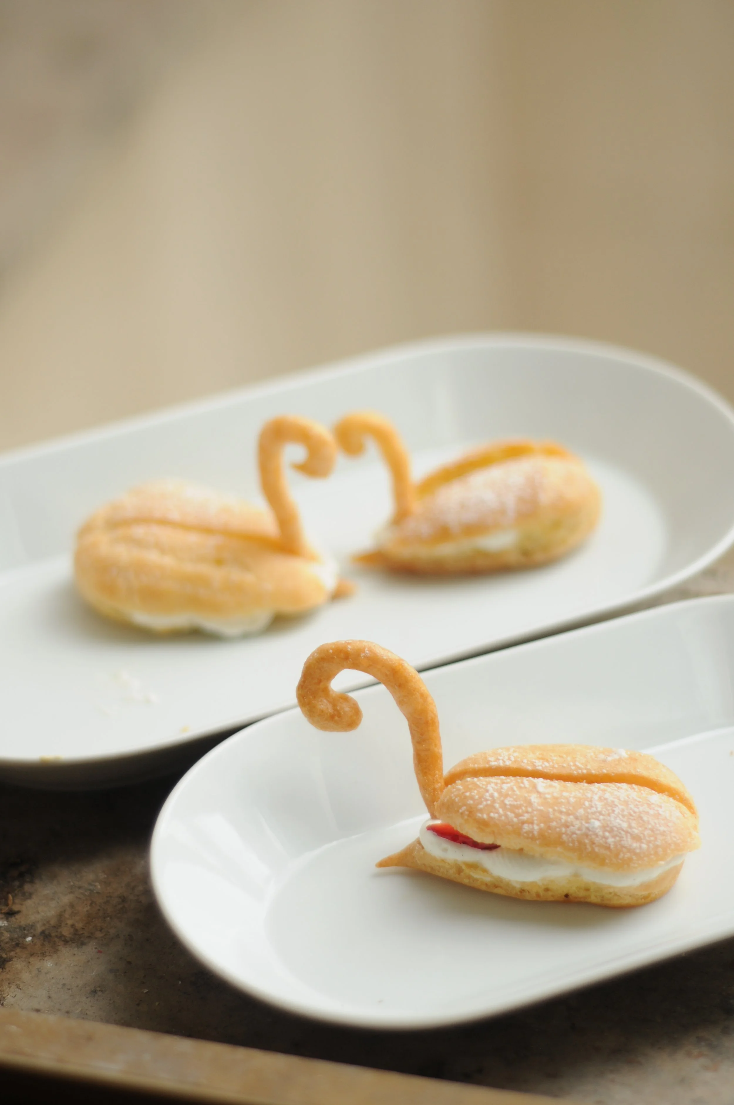 Desserts en forme de cygnes avec des ailes, garni de chantilly et fraises servis dans des assiettes blanches.