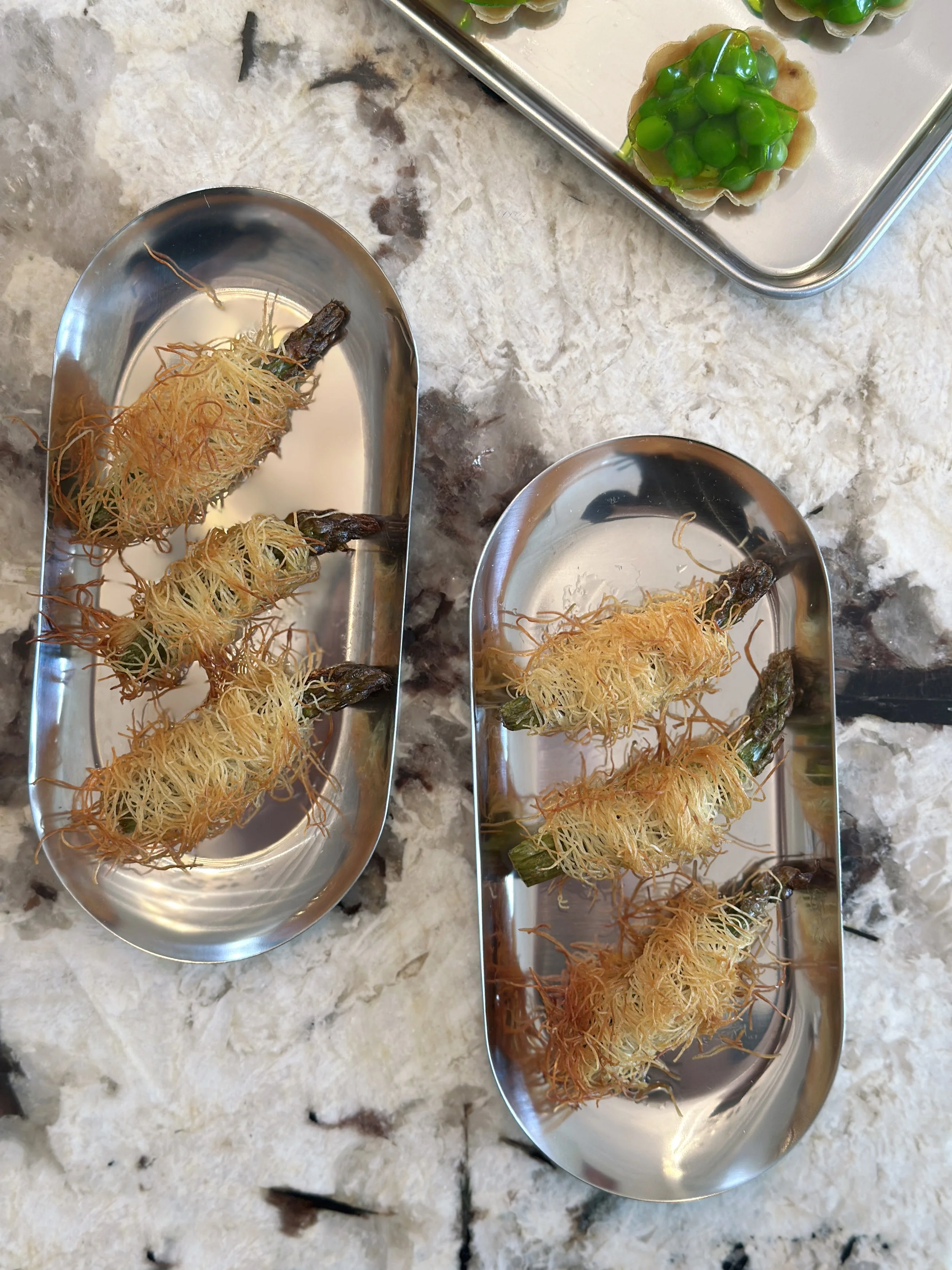 Croustillants en kadaïf avec des asperges vertes, placés sur des plateaux en métal.