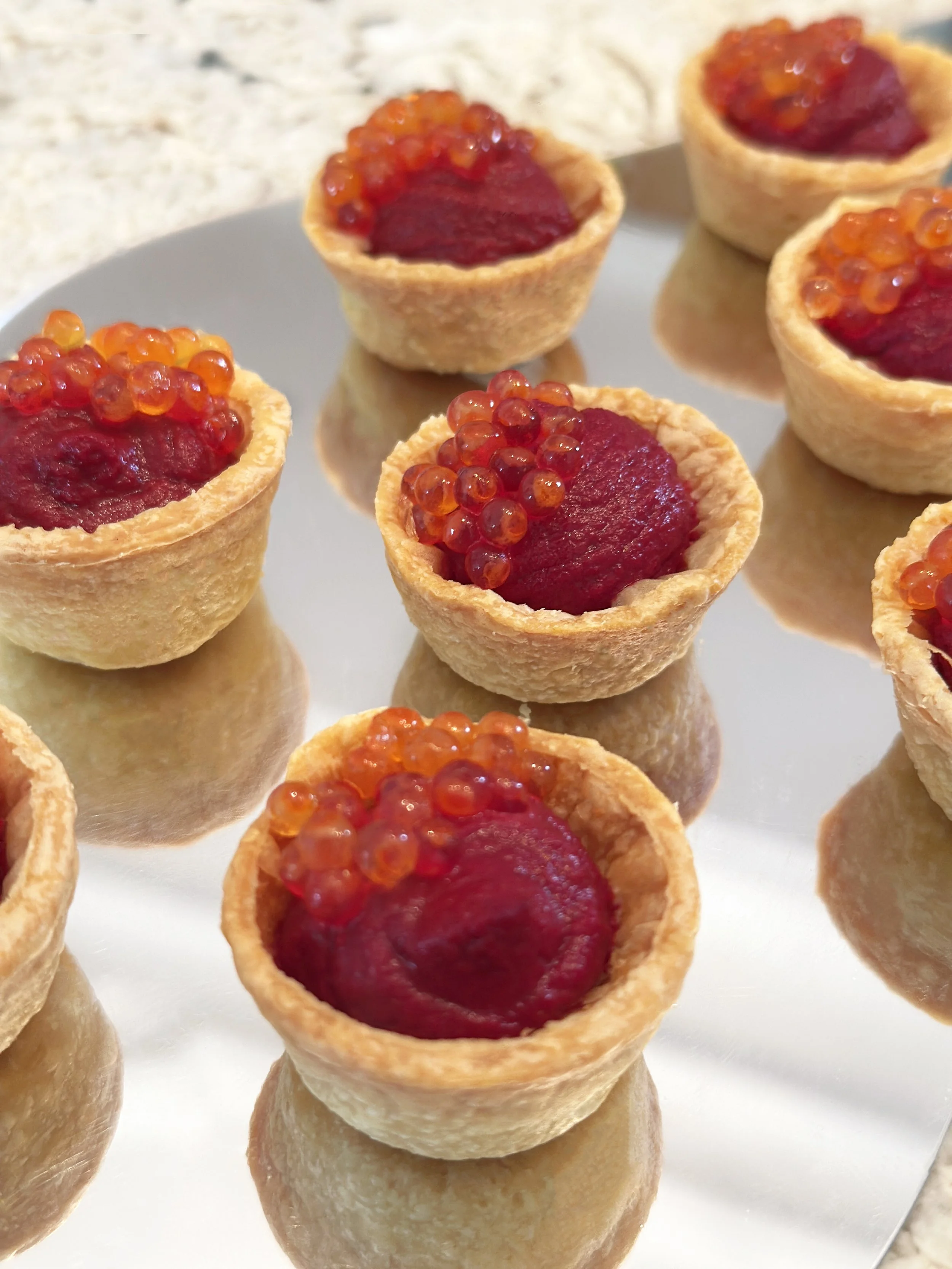 Petites tartelettes aux houmous de betterave et oeuf de truite, disposées sur une surface blanche.