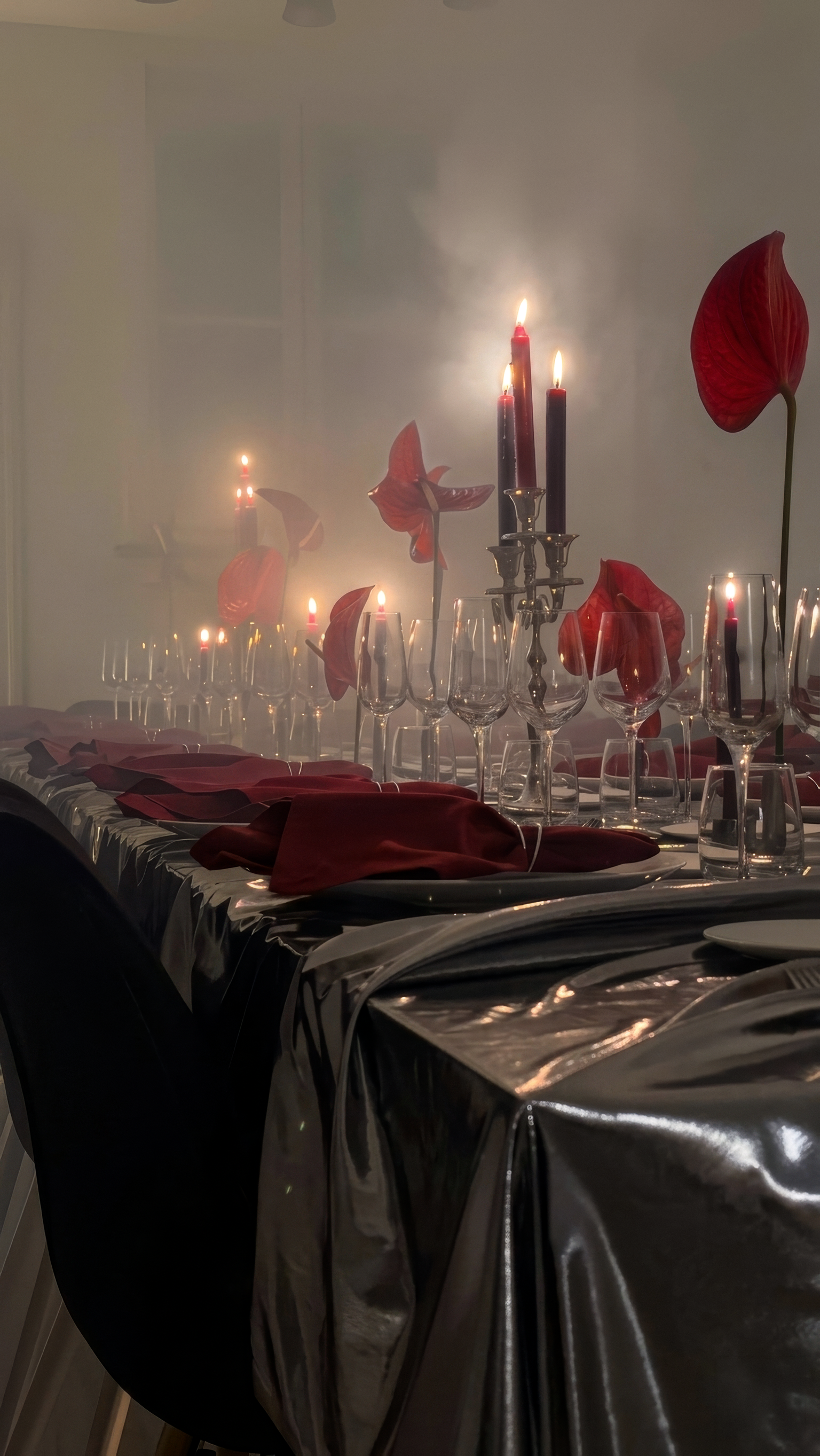 Table élégante avec de la vaisselle en verre, des bougies allumées dans des chandeliers, et des fleurs rouges, dans une ambiance chaleureuse et sophistiquée.