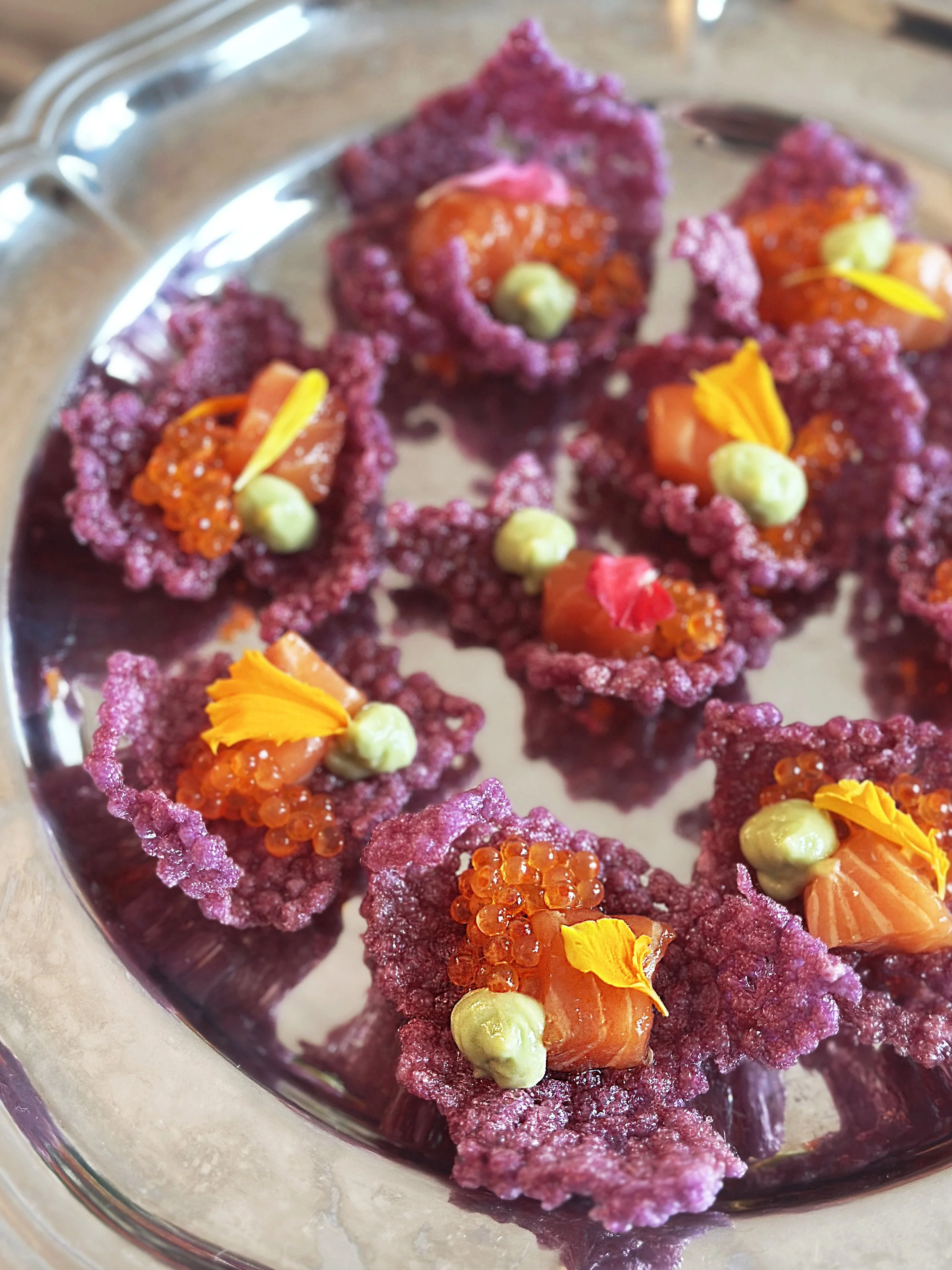 Cracker violet de tapioca soufflé en forme de fleurs, garnis de saumon, oeufs de truite et crème d'avocat, de pétales de fleurs.