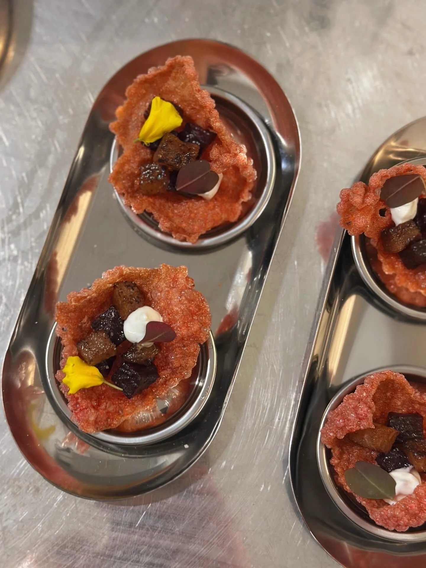 Petites portions de dessert dans des ramequins en acier inoxydable, garnies de garnitures variées, sur une surface en métal.