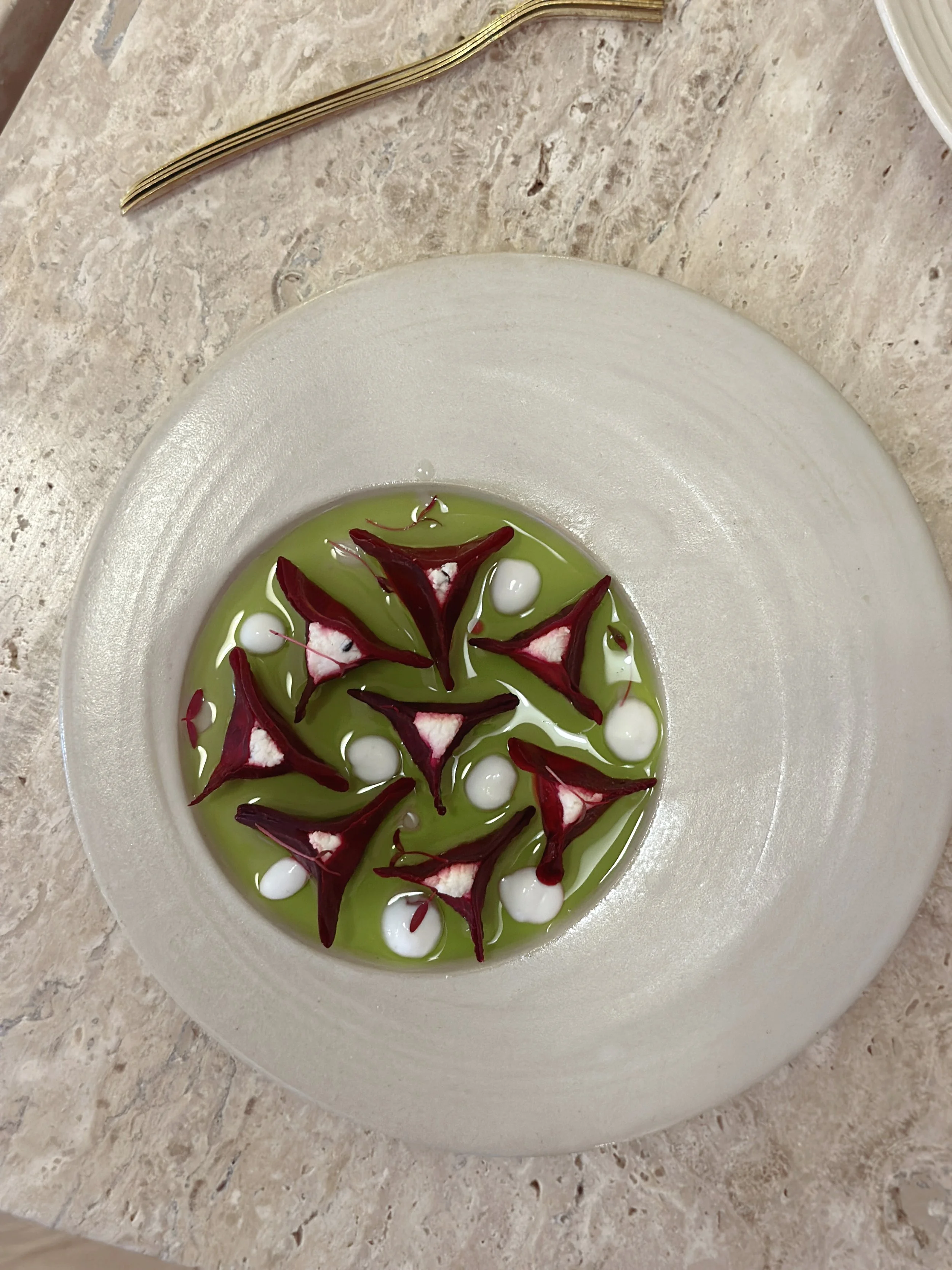 Une assiette de ravioles de betterave dans une huile verte, présentée de manière artistique.