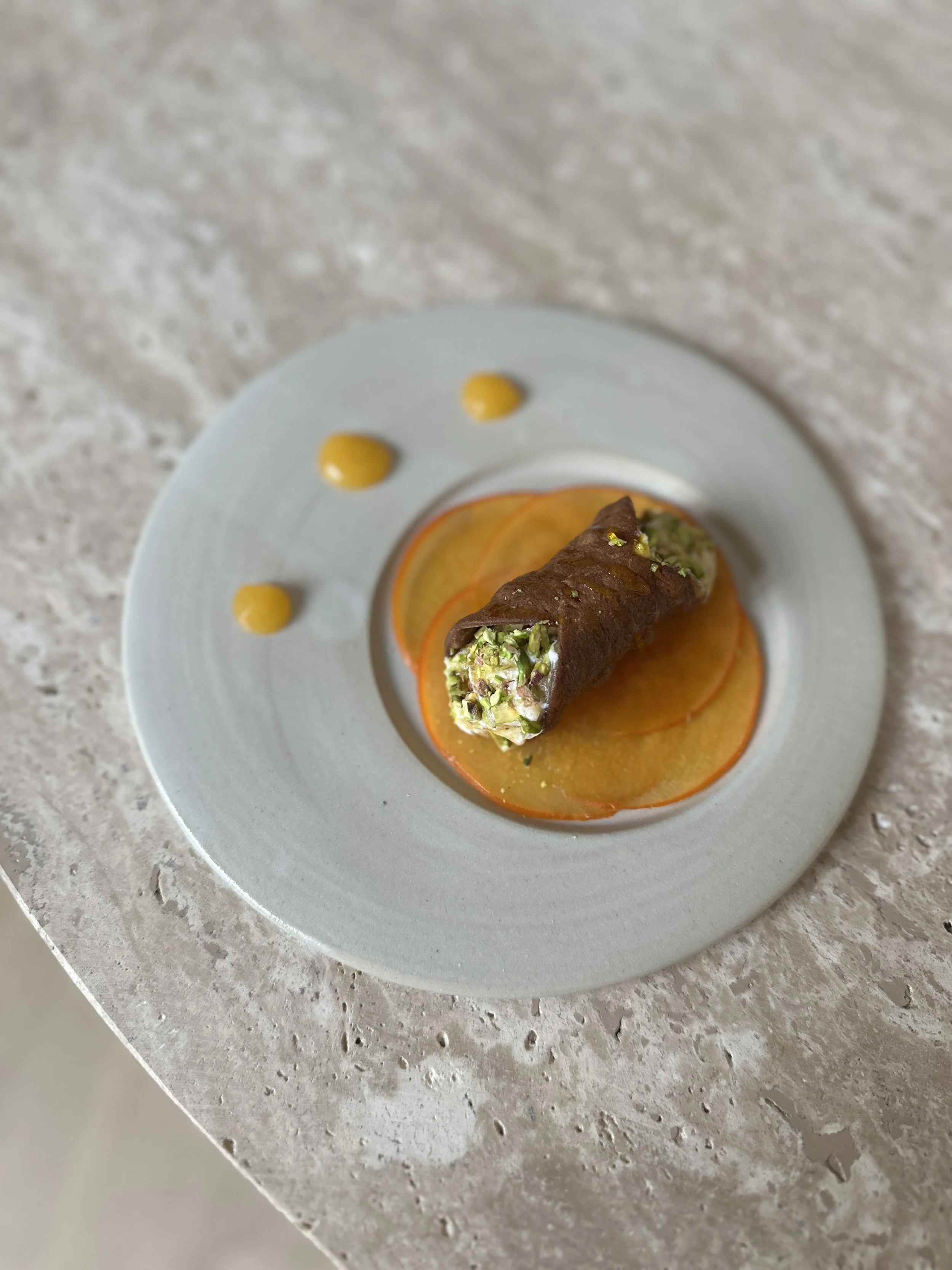 Cannoli sicilien avec du kaki, présenté sur une surface en pierre ou en marbre.