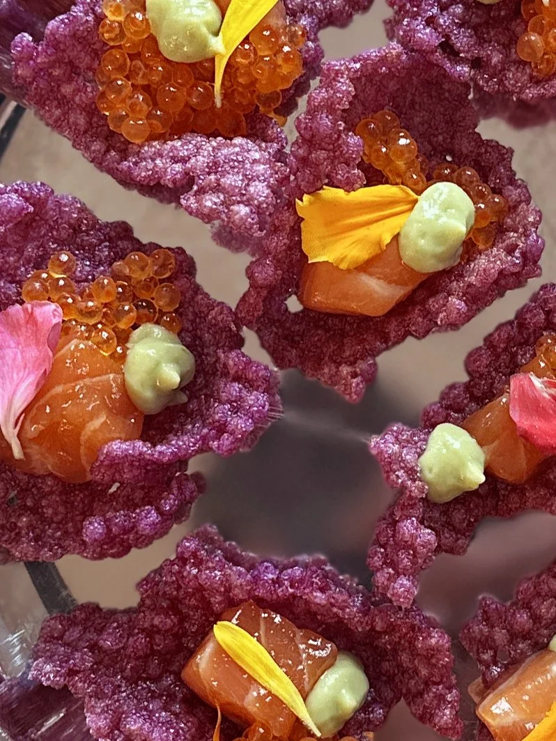 Cracker violet de tapioca soufflé en forme de fleurs, garnis de saumon, oeufs de truite et crème d'avocat, de pétales de fleurs.