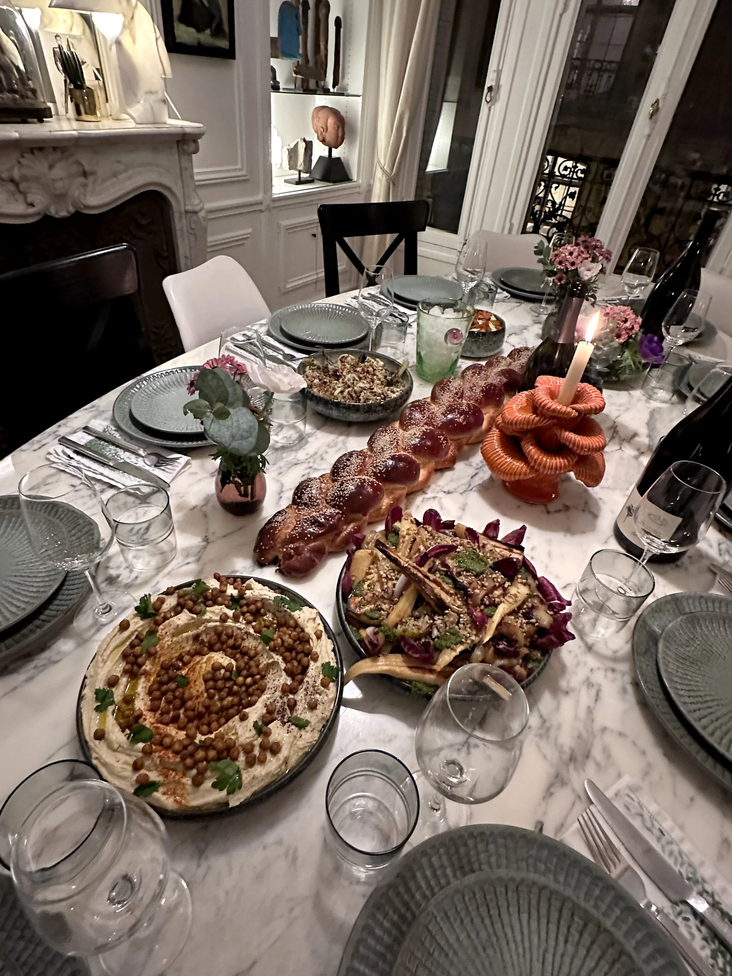 Une table festive avec des plats, des verres à vin, des décorations florales et une chandelle. La table est en marbre avec des assiettes, des couverts et des verres à vin.
