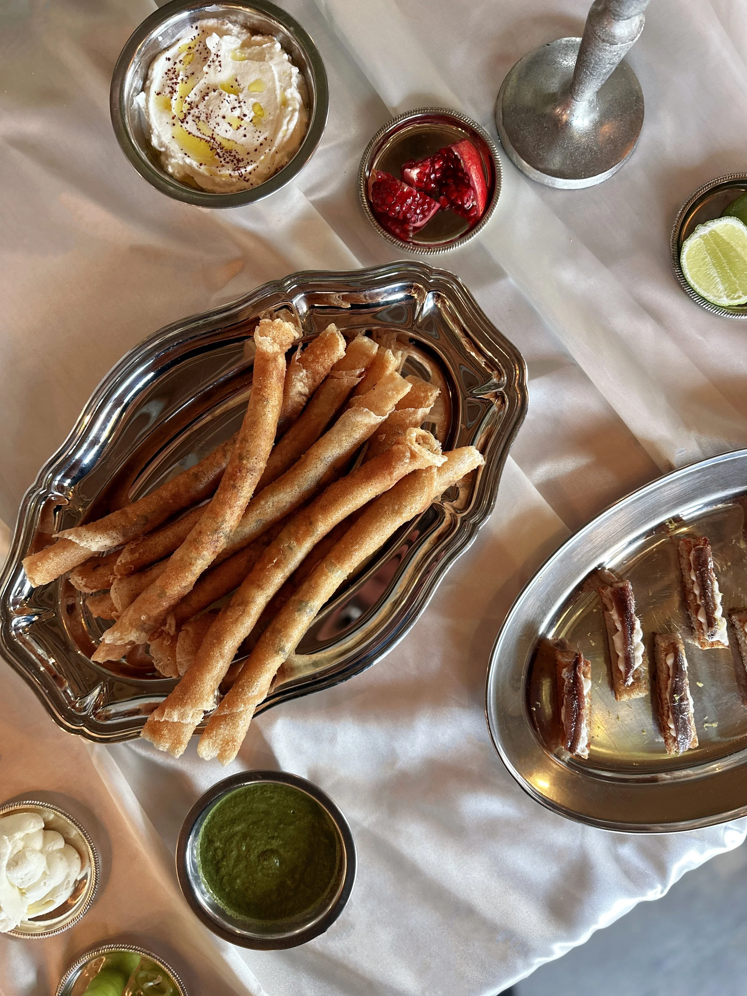 Cigares de poisson avec sauce au yaourt et zhug une coupe de pomegranate et des lime, présenté sur une nappe blanche.