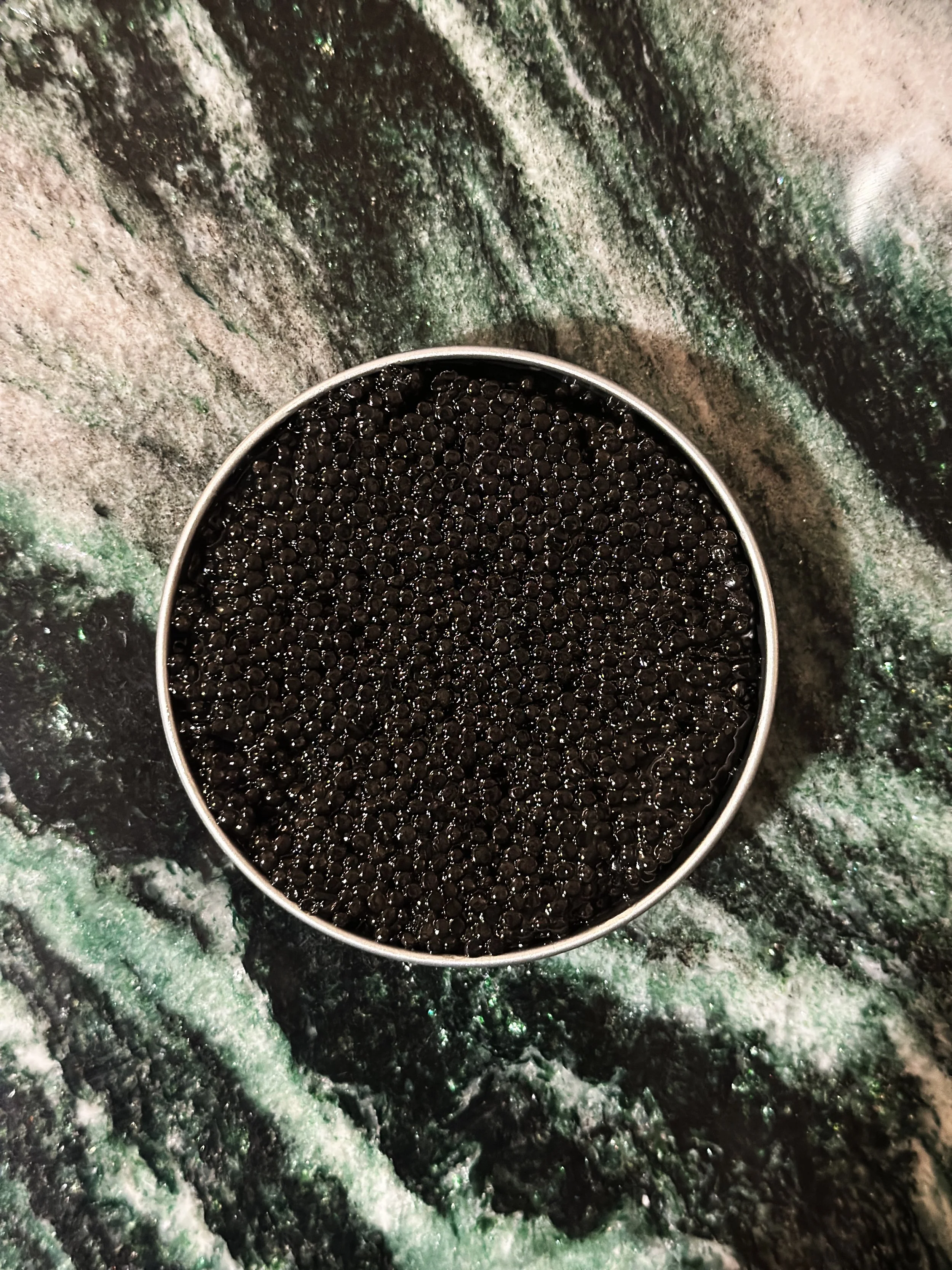 Une boîte métallique de caviar sur table en marbre vert.