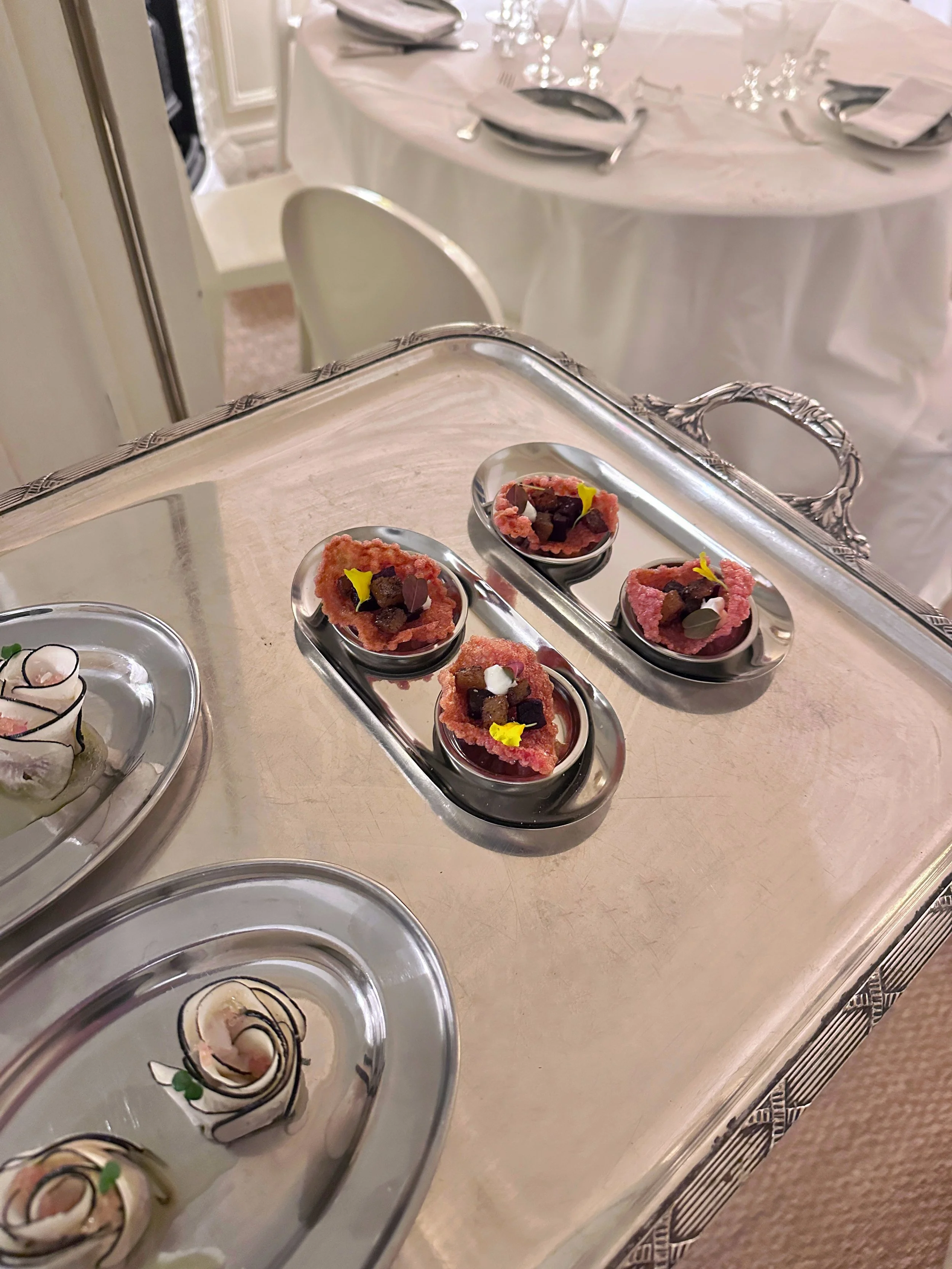 Desserts élégants et fins placés dans de petites cuillères en métal, sur un plateau en argent, dans un cadre de salle de réception ou de banquet.