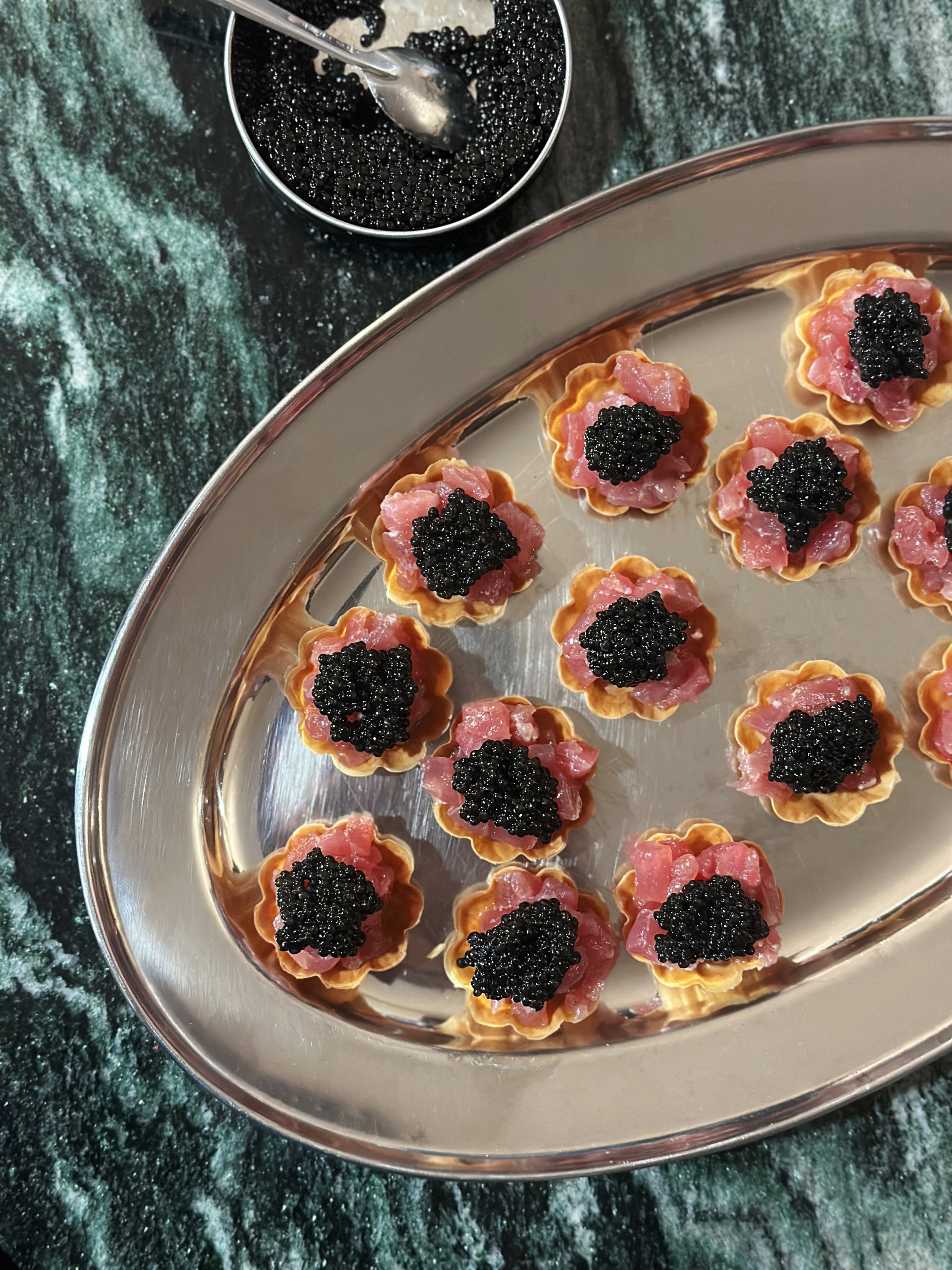 Petites tartelettes de tartare de thon rouge et caviar, alignées sur un plateau en métal.