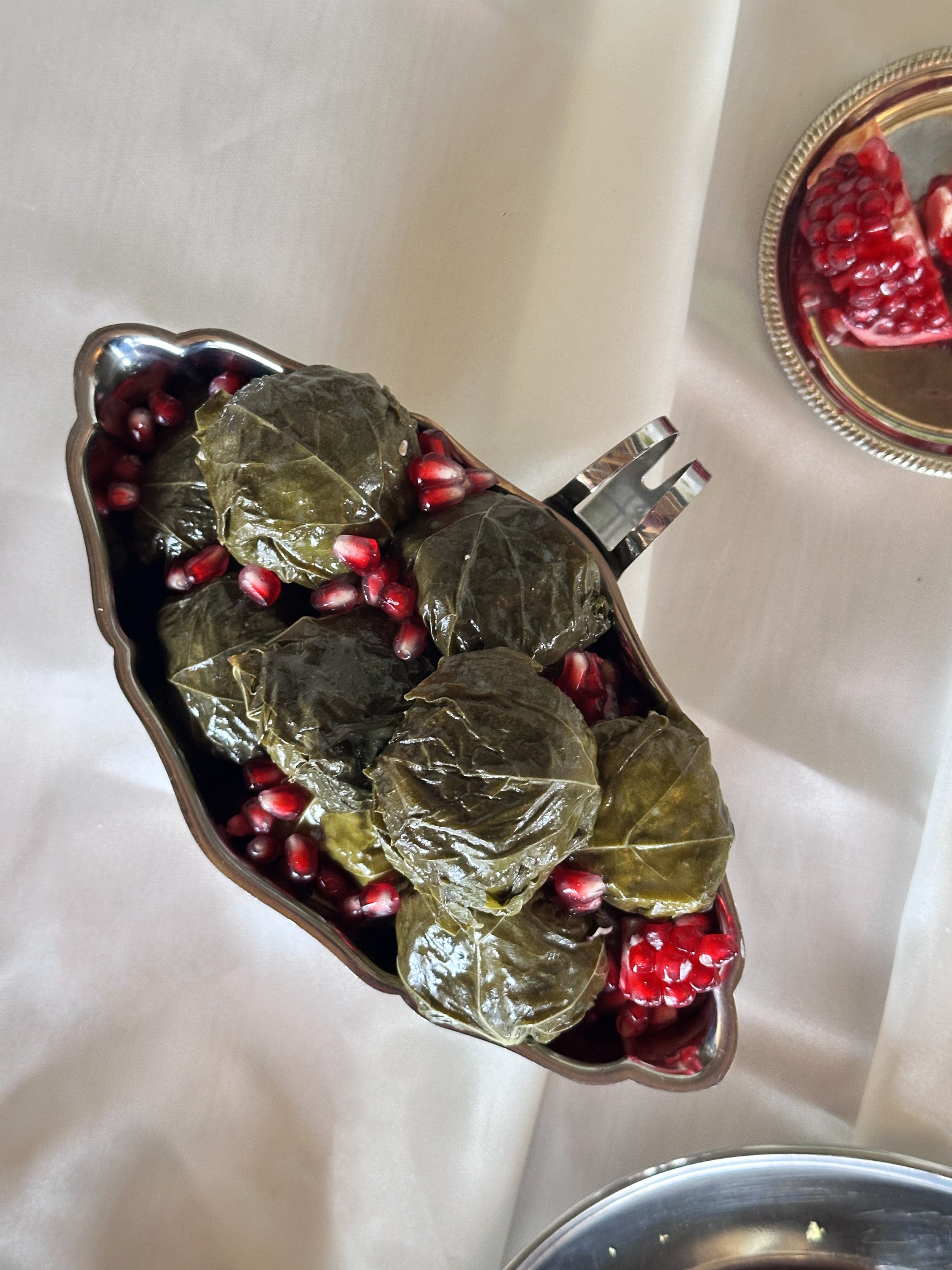 Boules de feuilles de vigne garnies, avec des graines de grenade, et une petite assiette de morceaux de grenade à côté.