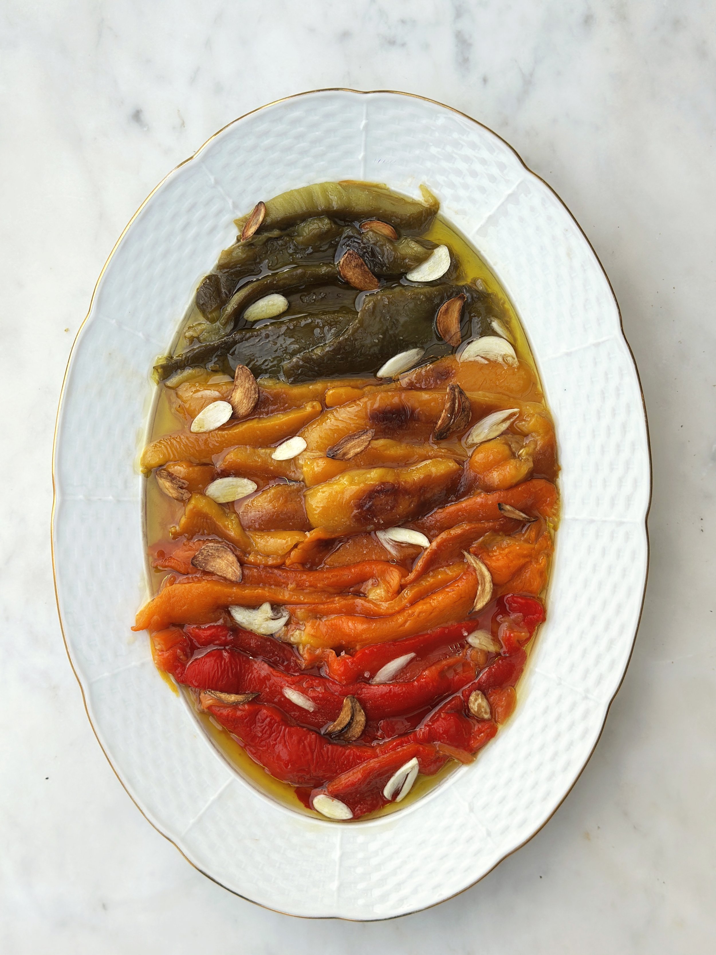 Assortiment de poivrons farcis de différentes couleurs (vert, orange, rouge) servis avec une sauce à l'huile d'olive et garnis de graines de courge.