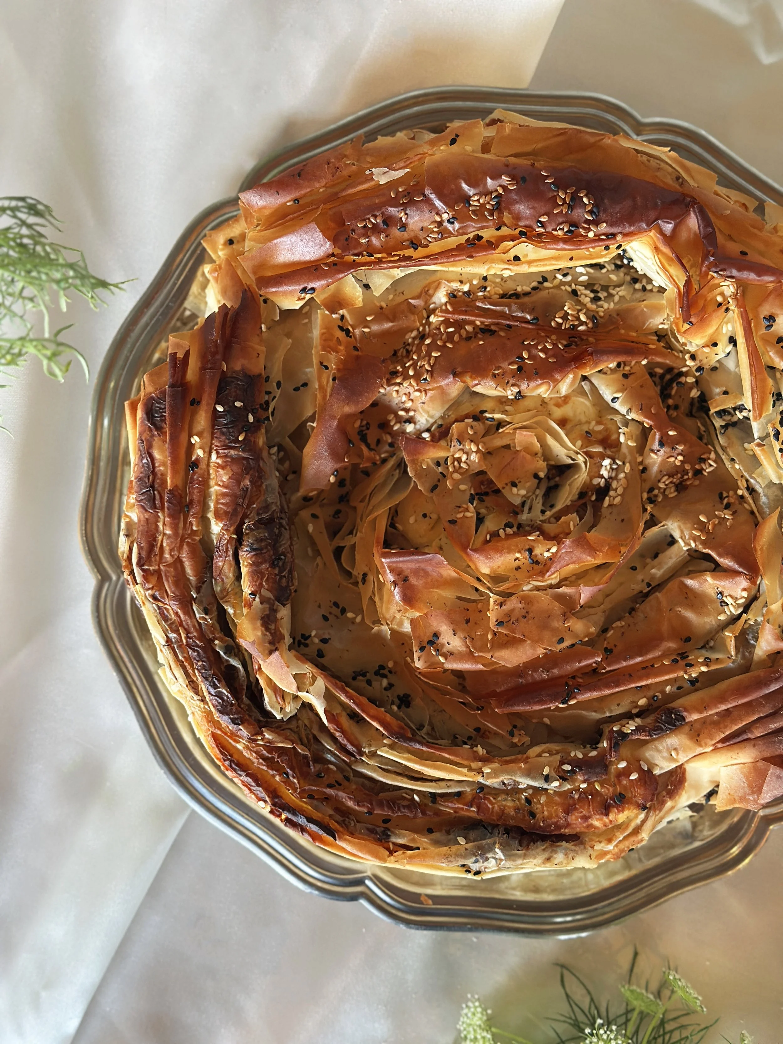 Spanakopita, décorée avec des graines de sésame noir et blanc, dans un plat en inox.