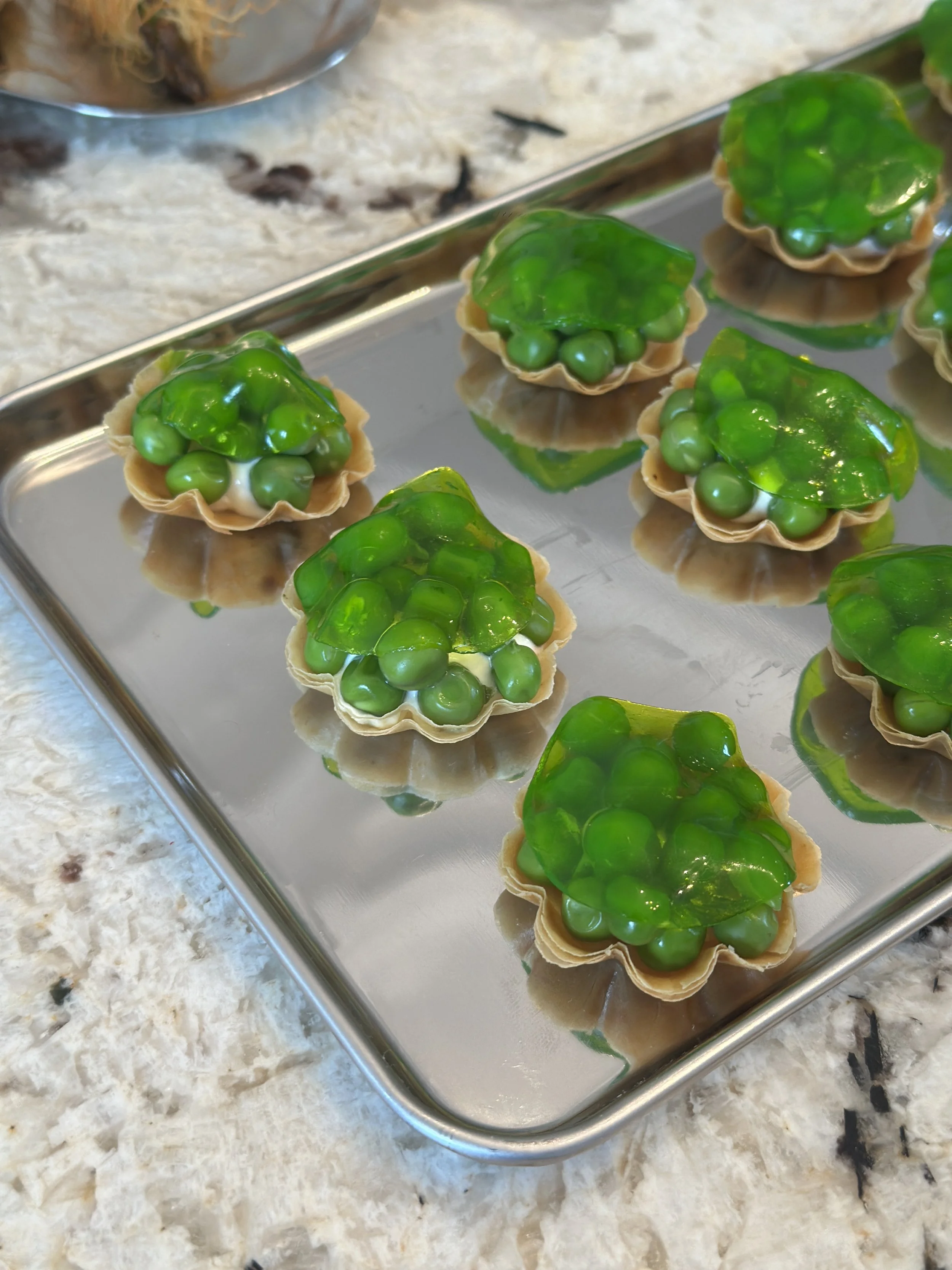 Tartelettes petit pois avec une garniture verte brillante sur une plaque en métal, posée sur un plan de travail en marbre.