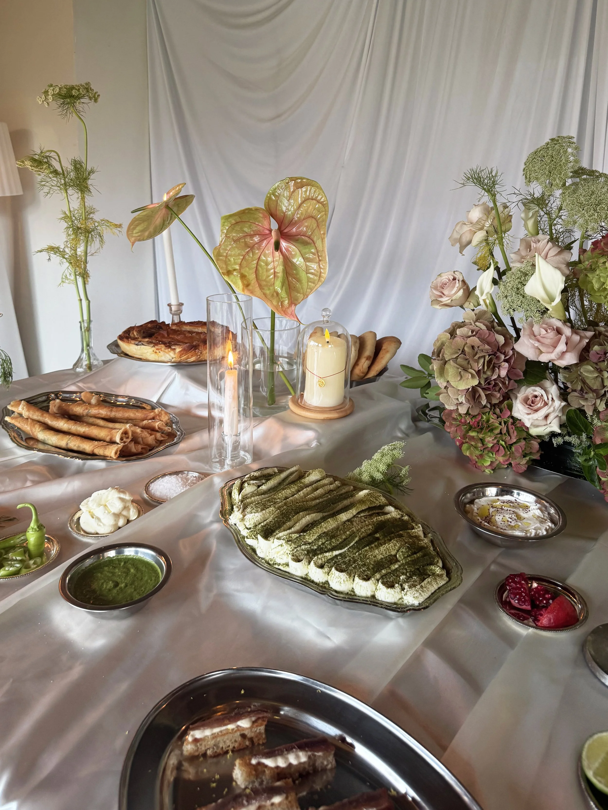 Table dressée avec plusieurs plats, sauces, et fleurs décoratives dans un cadre intérieur avec un fond de toile blanche.