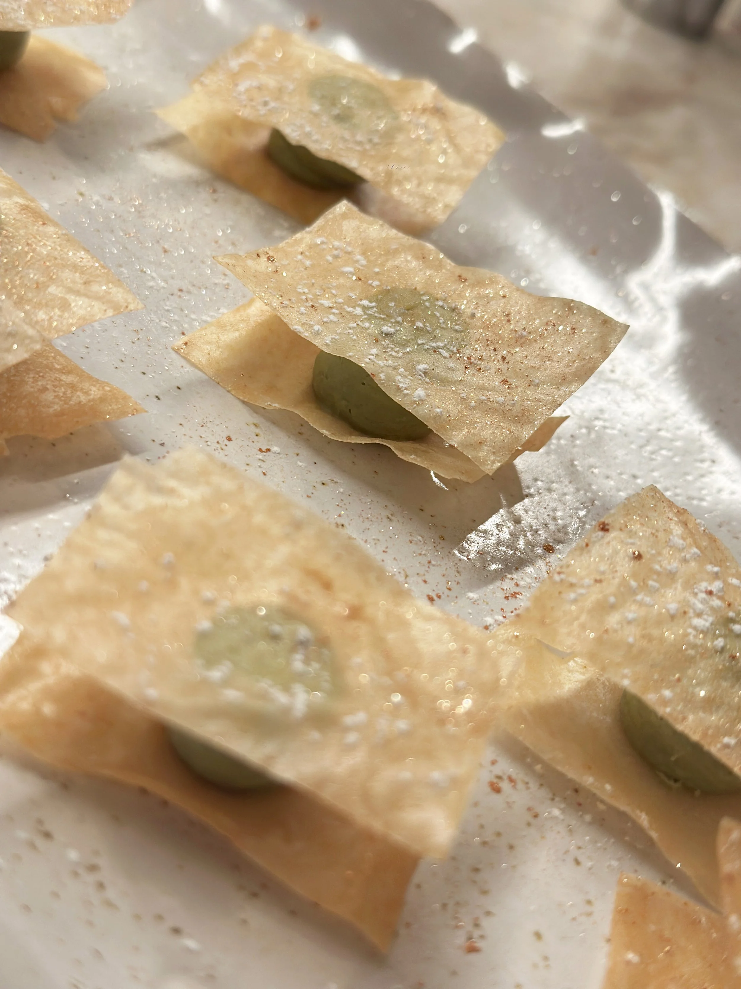 Gros plan sur des feuilles de pâte ou de papier de cuisson avec des grains verts à l'intérieur, saupoudrées de farine ou d'épices, semblant être des raviolis ou des dumplings.