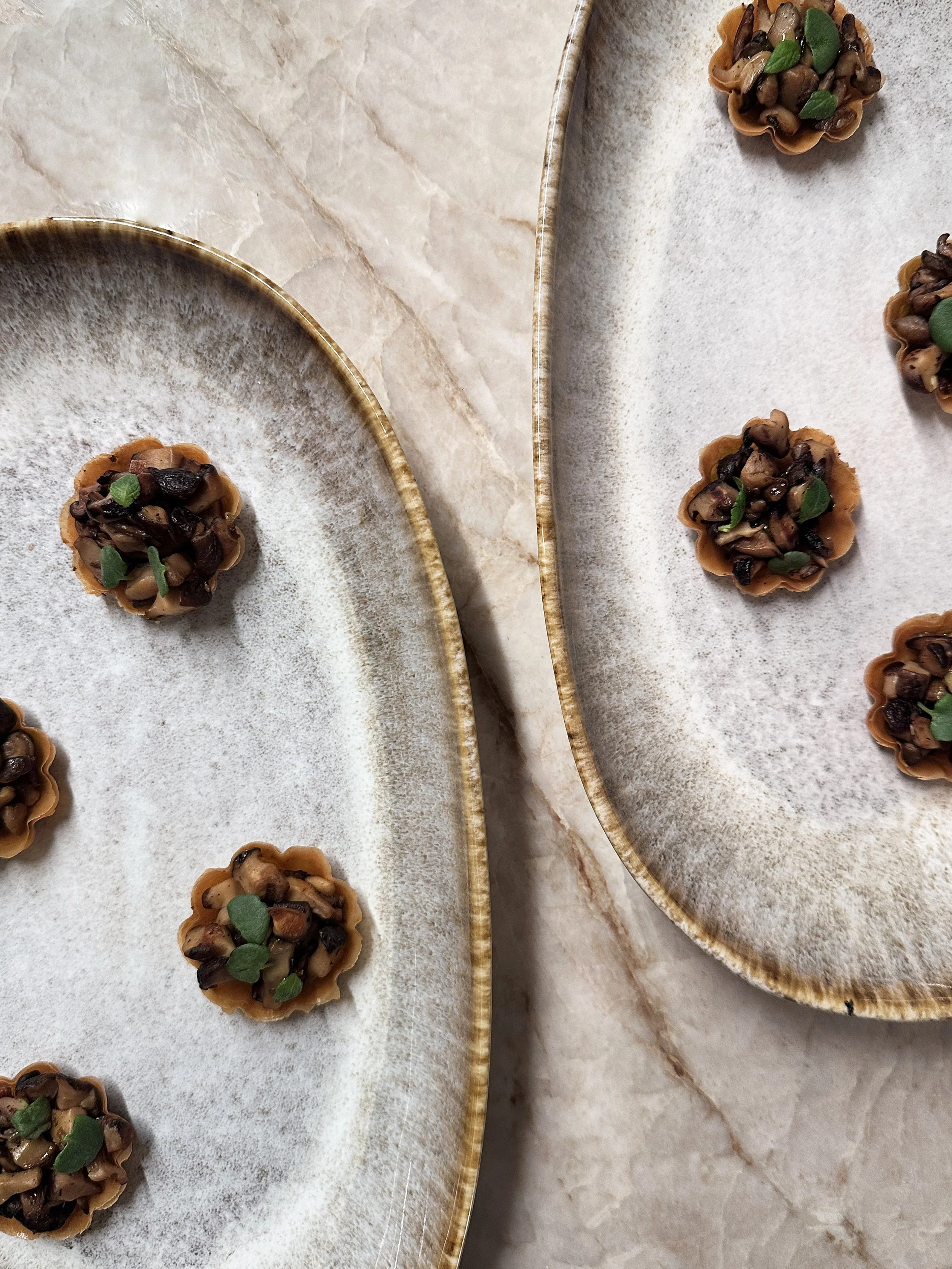 Tartelettes avec une garniture composée de champignons et de petites feuilles de basilic, disposées sur une plaque en céramique.