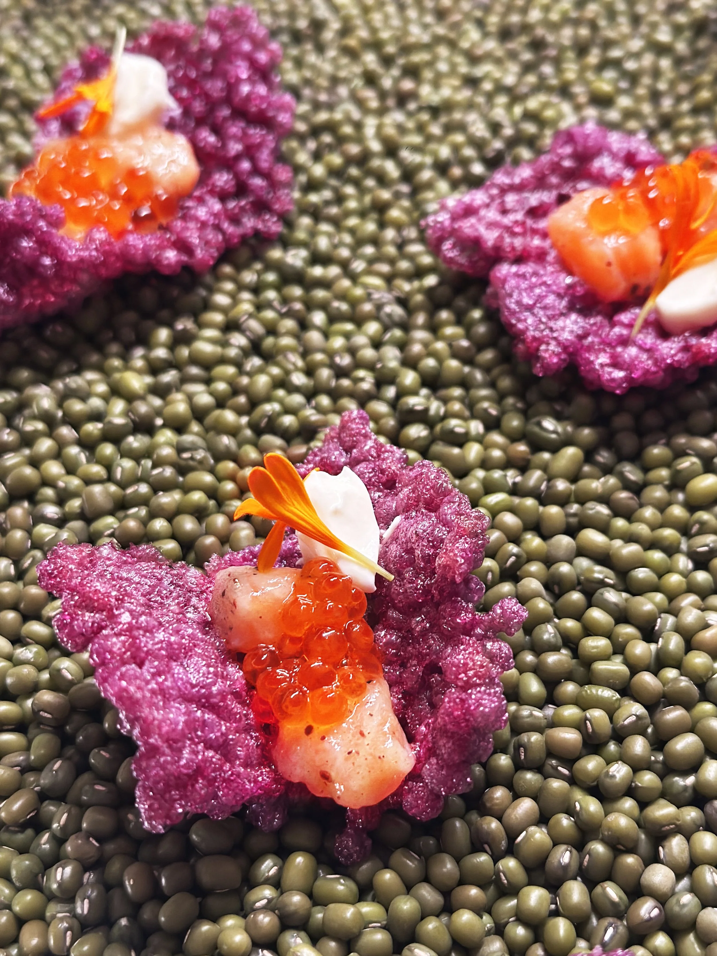 Cracker violet de tapioca soufflé en forme de fleurs, garnis de saumon, oeufs de truite et crème, de pétales de fleurs.