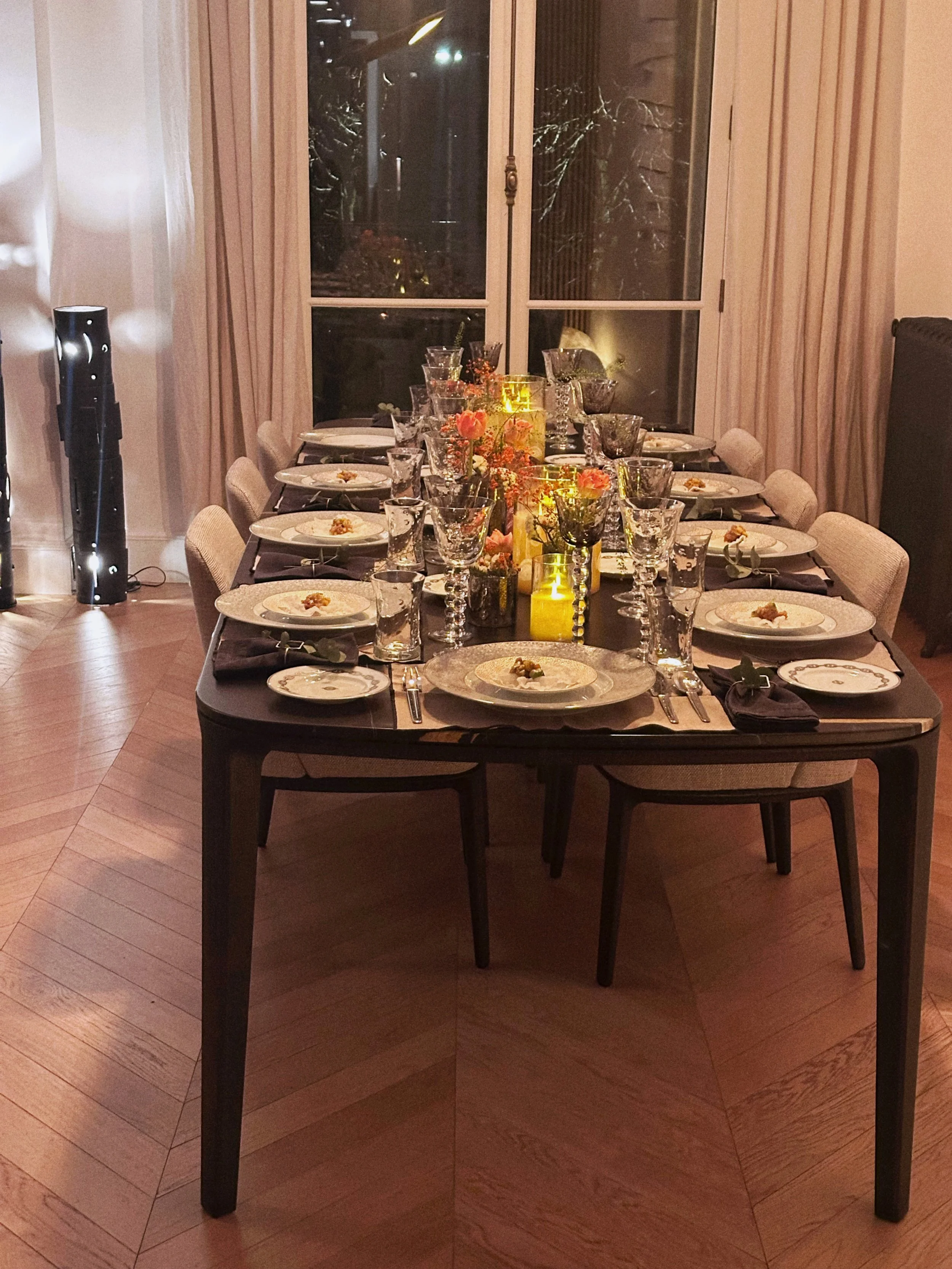 Une table élégante dressée pour un repas, avec des assiettes, des verres à vin, des couverts, des bougies et des fleurs dans des vases, dans une salle à manger chaleureuse.