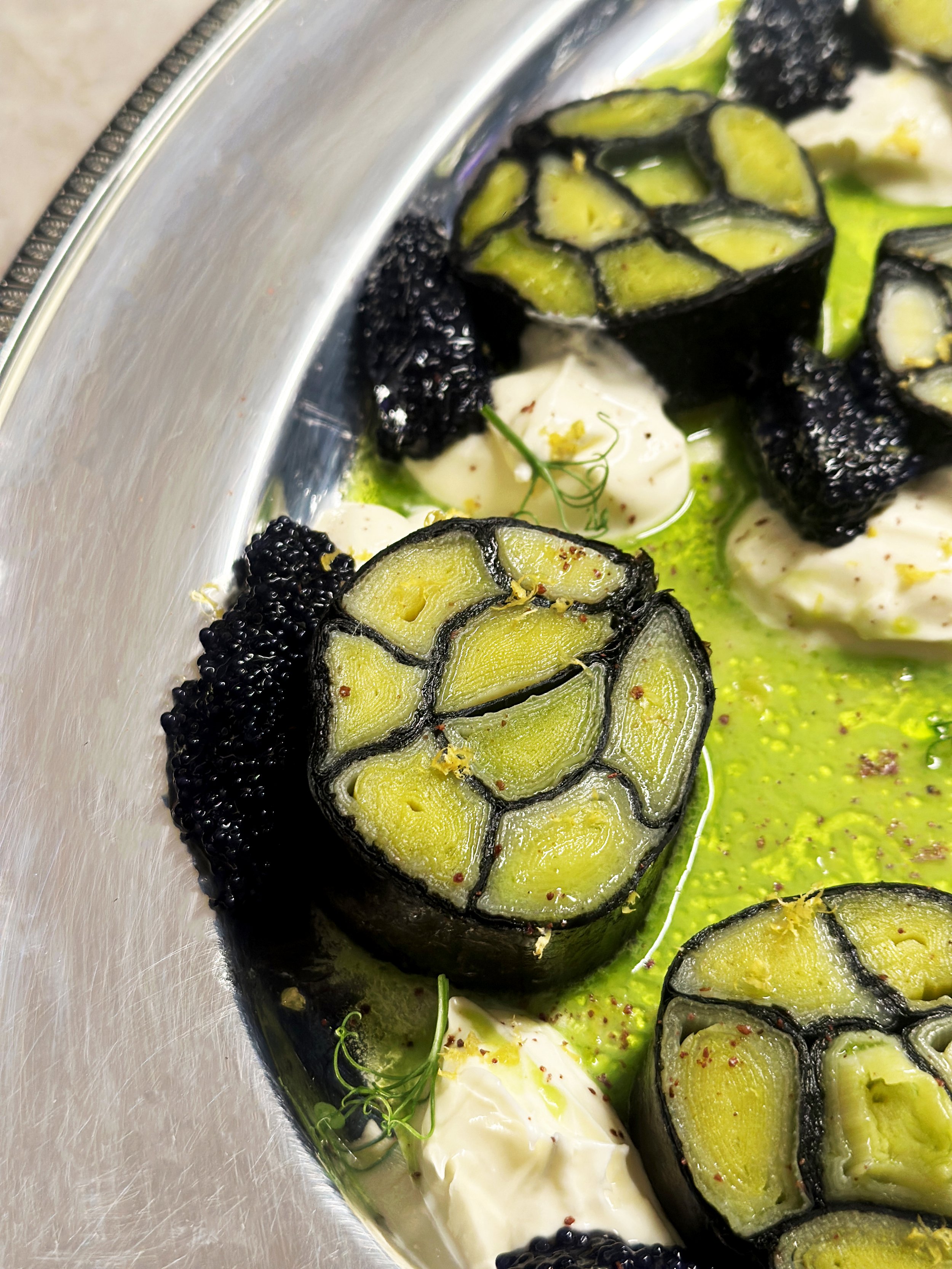 Mosaïque de poireau avec oeuf de lomp noir et crème, huile de poireau, dans un plat en métal