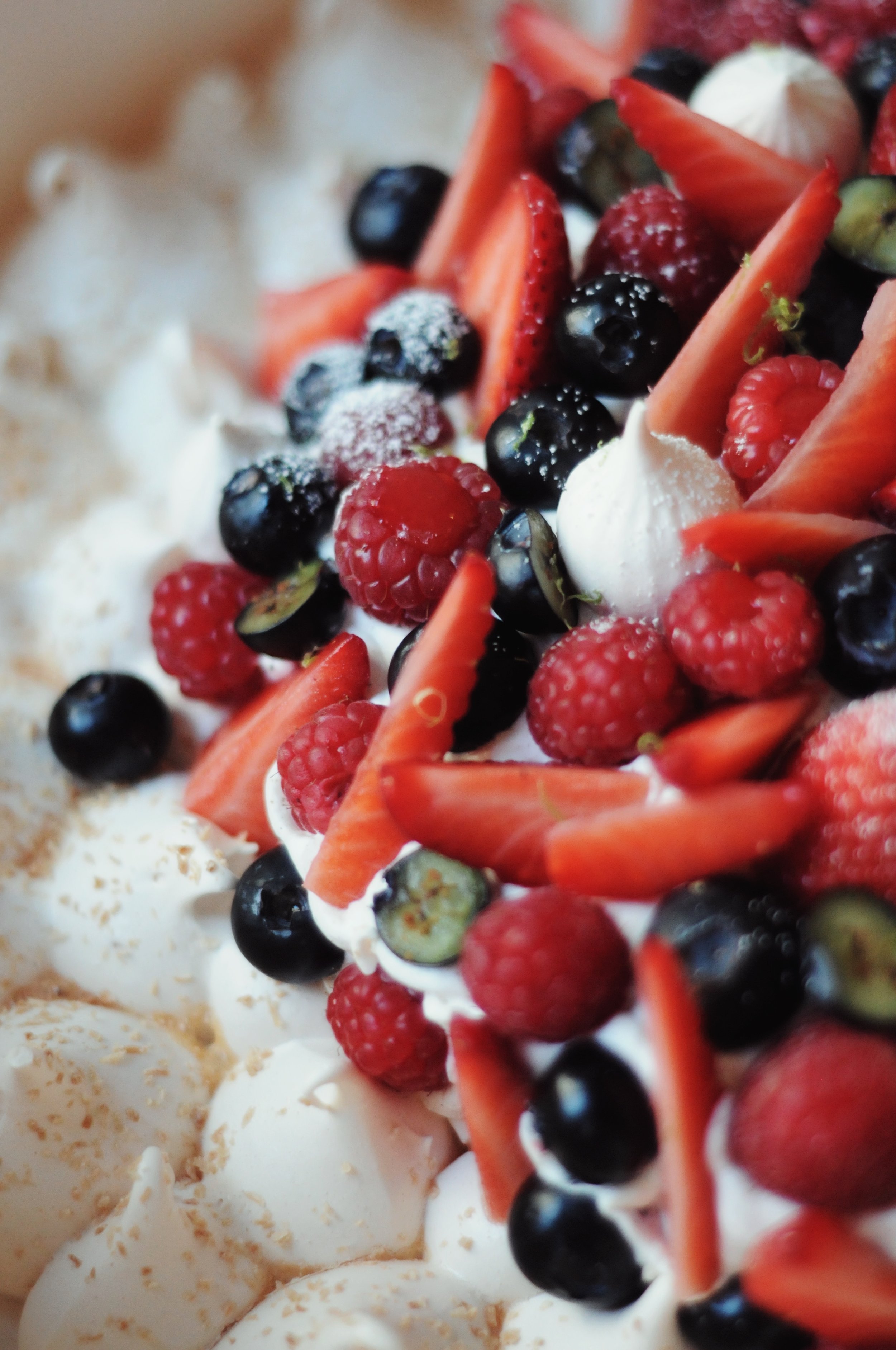 Gros plan d'une pavlova décorée de fruits rouges tels que framboises, mûres, fraises et des morceaux de meringue, avec de la crème 