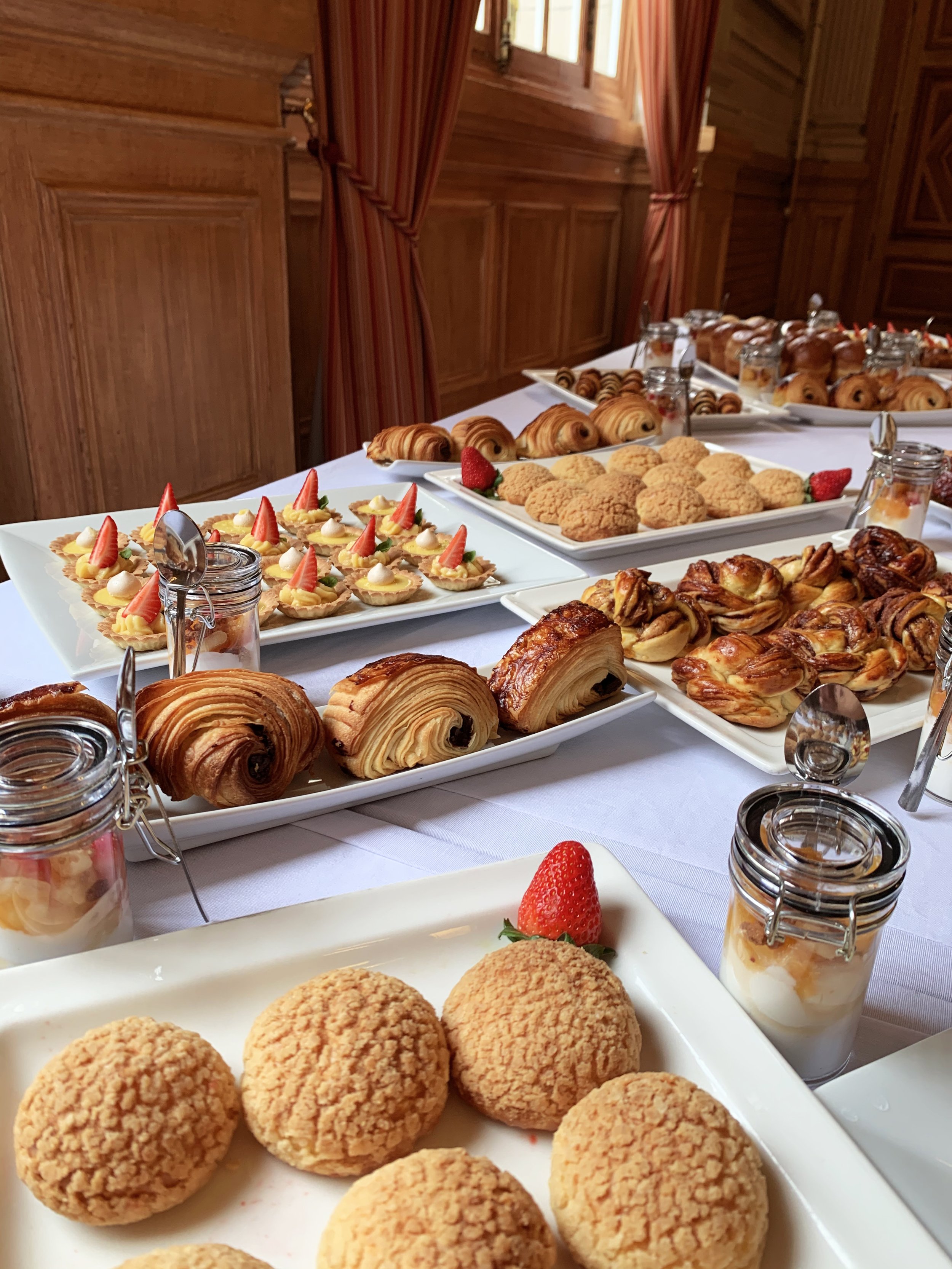 Table de desserts avec cookies, pastries, tartelettes, et verrines de pudding, dans une salle en bois.