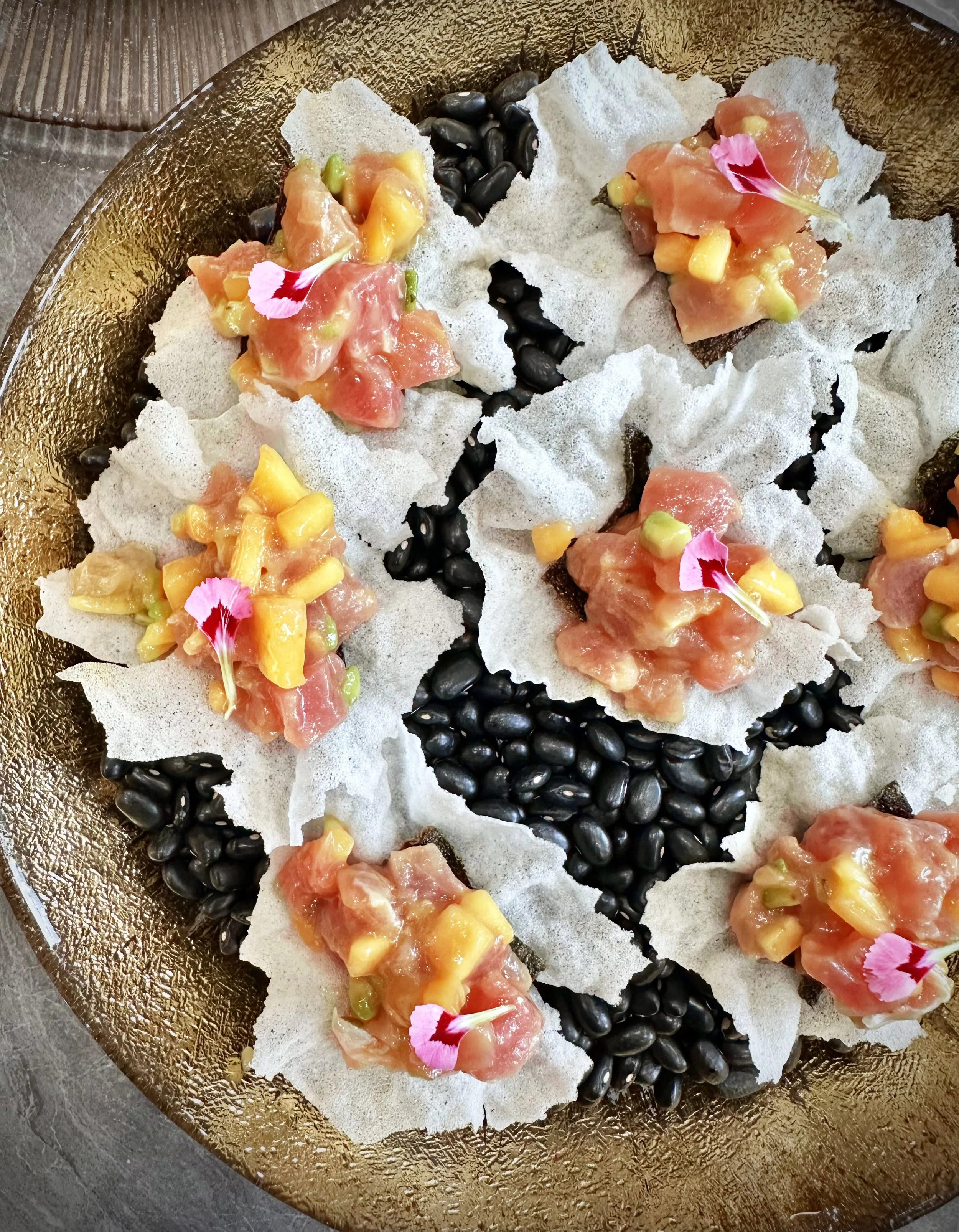 Plate en or avec des de fines feuilles de riz croustillantes garnies de tartare de thon, décoré de fleurs roses comestibles.