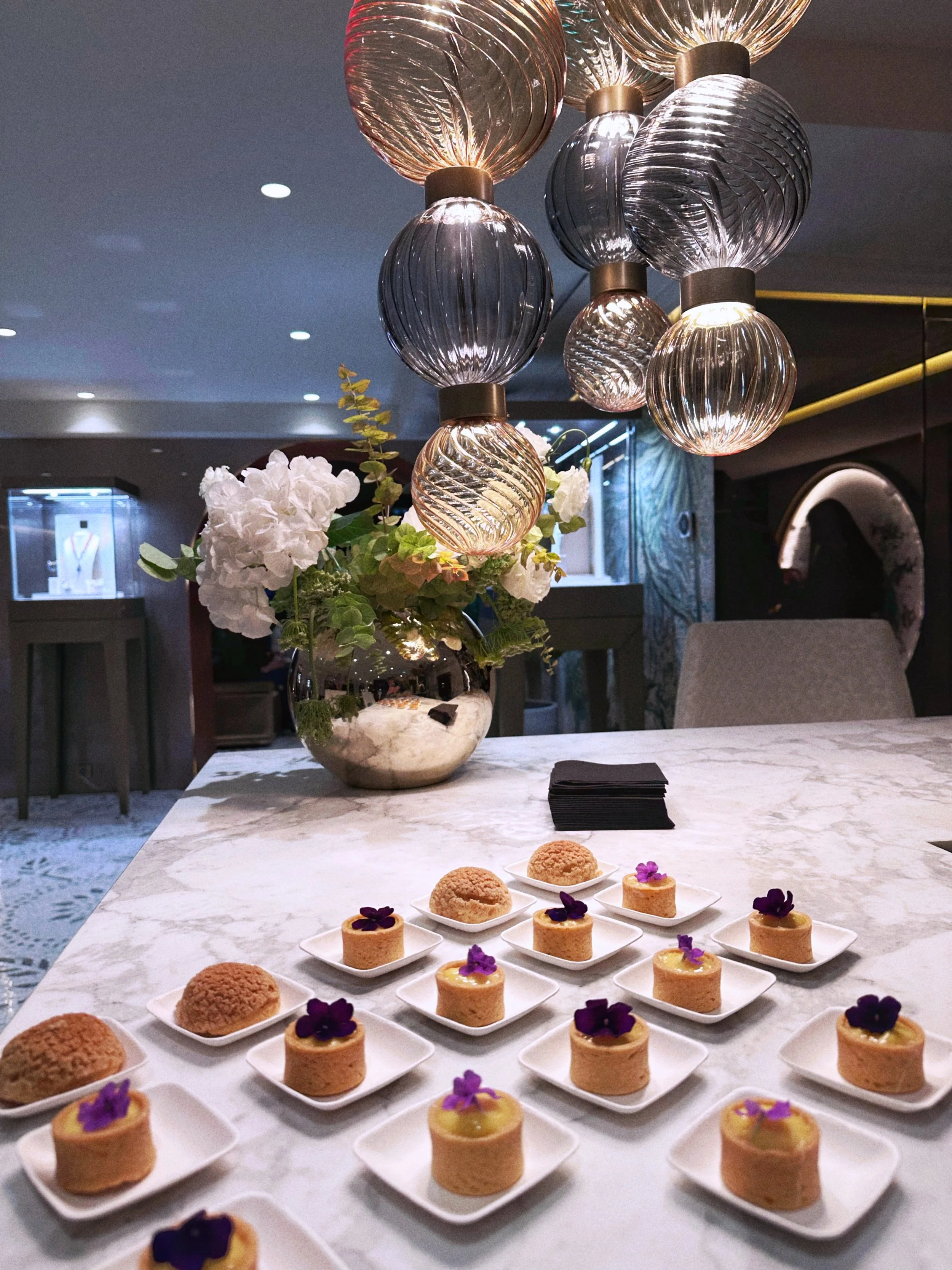 Desserts mini tartelettes au citron avec des fleurs violettes sur une table en marbre blanc.