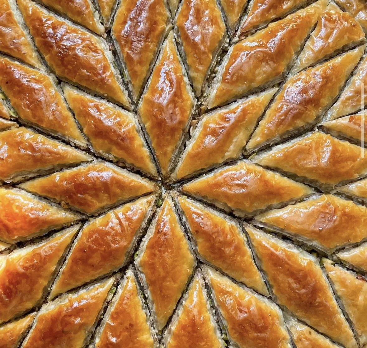 Baklava en forme de pyramides dorées, probablement une pâtisserie ou un baklava, présenté en rangées bien alignées.