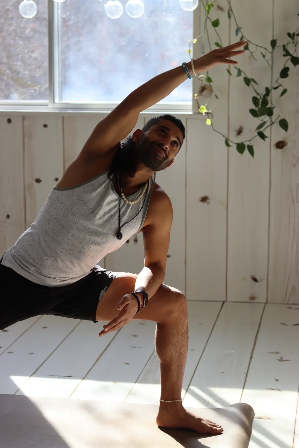 A man practicing yoga indoors, in a low lunge pose, reaching upward with his right arm and looking toward the ceiling.