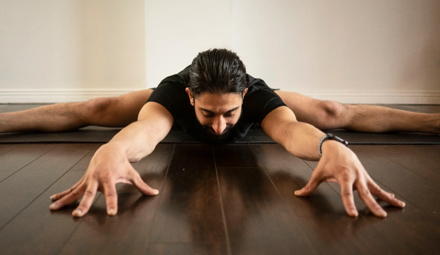 Man stretching on the floor in a yoga pose with arms extended forward and legs spread apart.