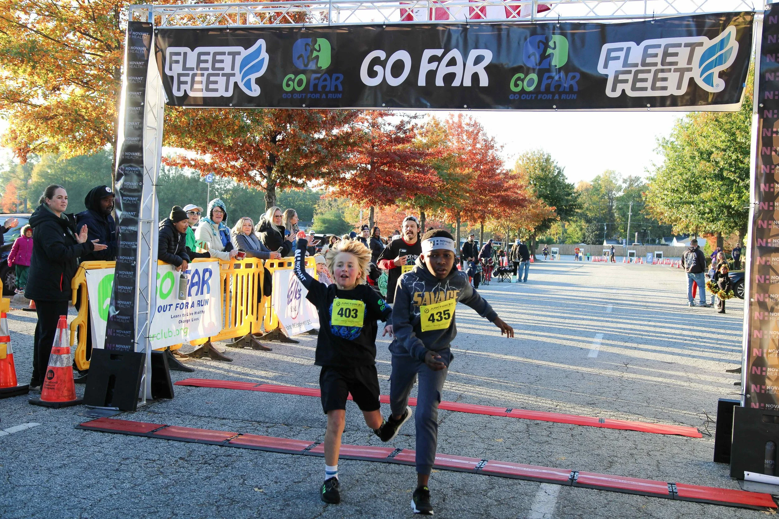 Children running in a race crossing the finish line at an outdoor event during autumn.