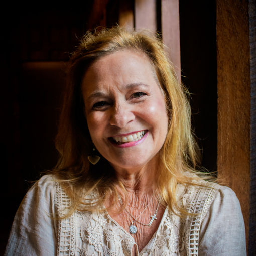 A woman with blonde hair smiling in front of a wooden background.