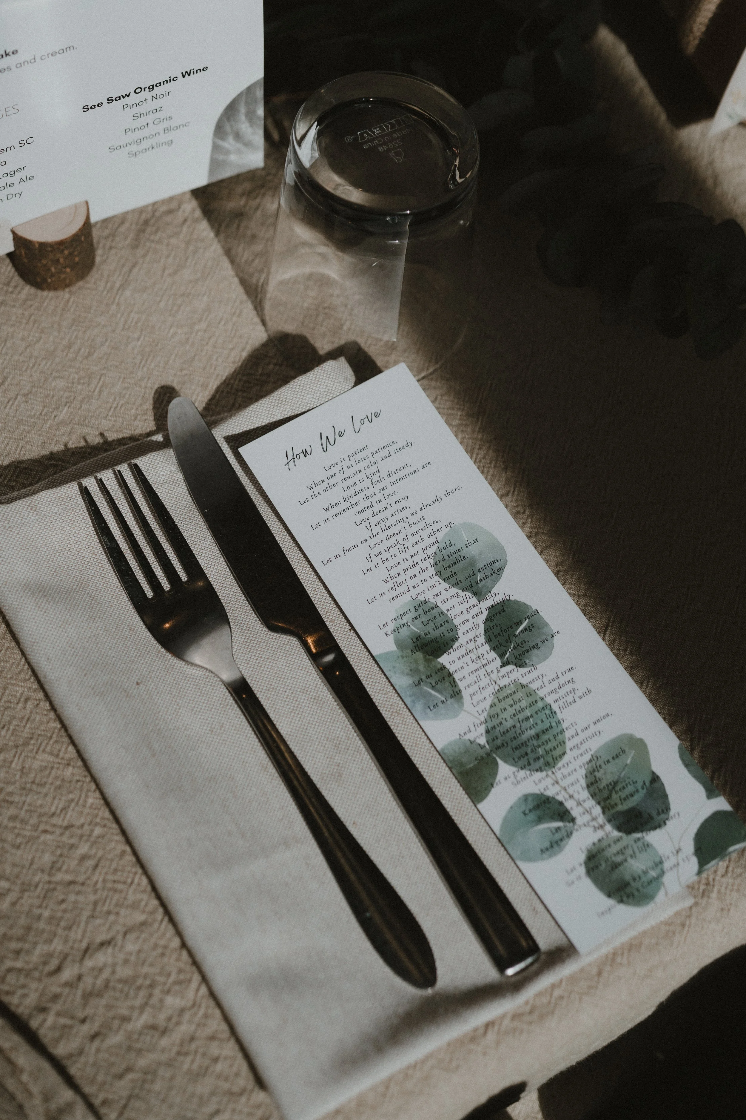 Elegant wedding table setting with cutlery on a white napkin, a glass of water, and printed menu cards with green watercolour designs, representing a refined celebration of love and a meaningful, committed relationship.