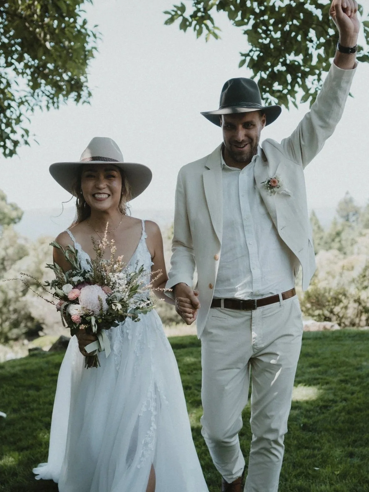 Smiling bride and groom walking hand in hand outdoors at a wedding, surrounded by greenery, representing a joyful, committed, and lasting relationship.