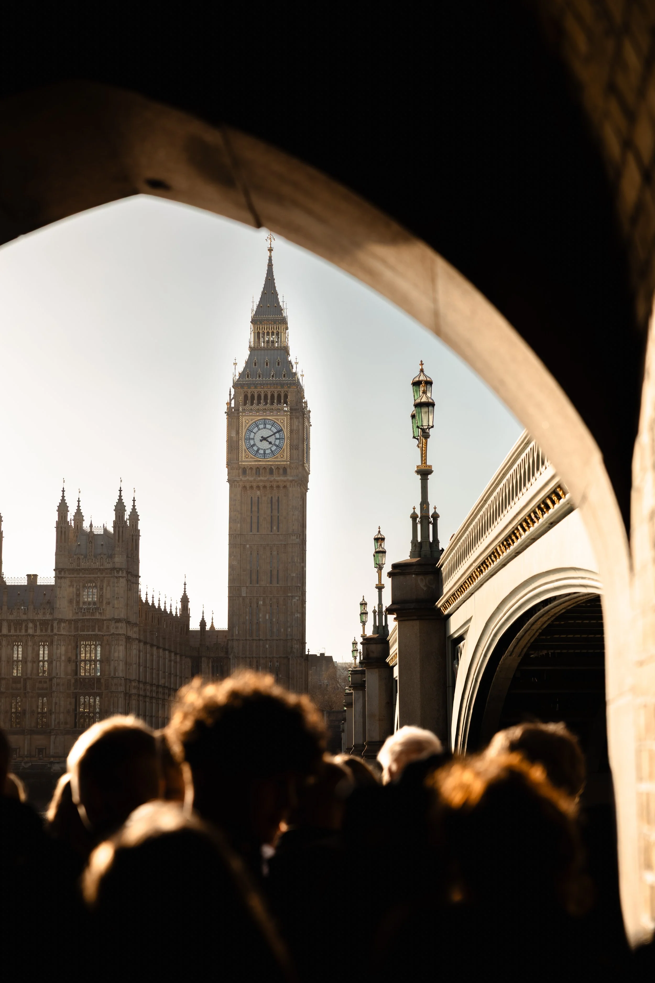 Big Ben shines in the sunlight, with people in the foreground beneath an arched tunnel.
Taken in London