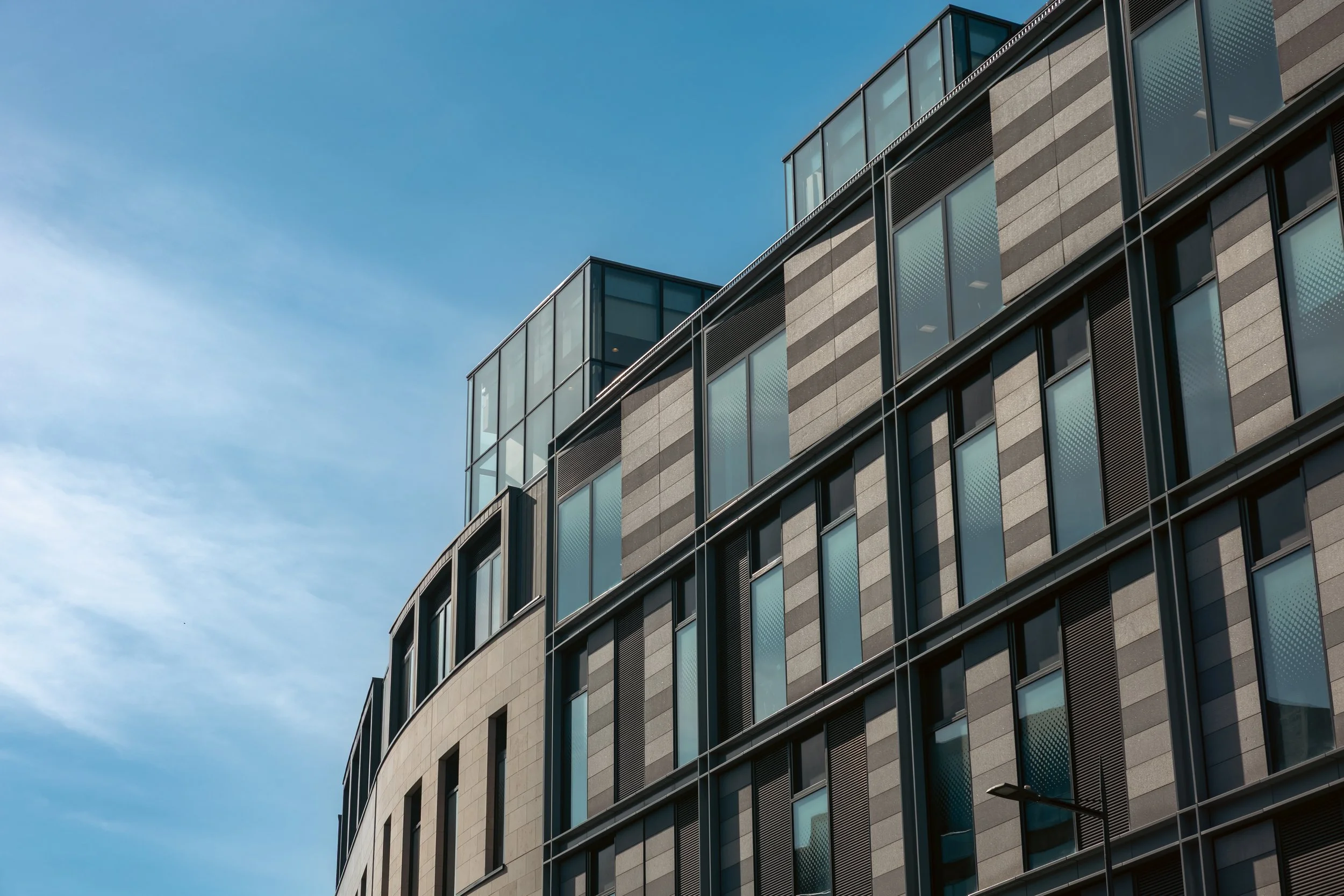 Modern multi-story building with large glass windows under a blue sky.