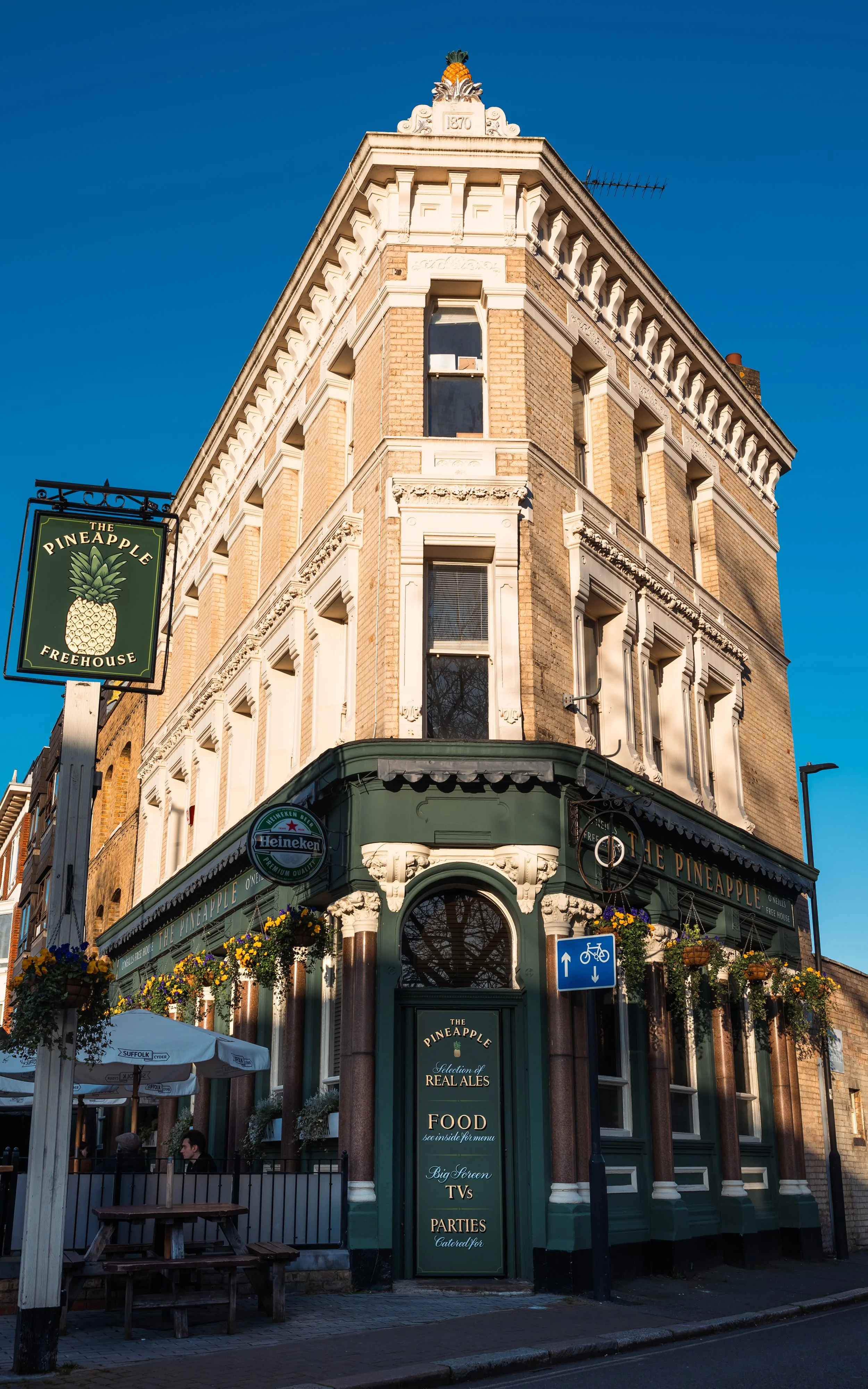 A multi-story brick building with ornate white trim, featuring a corner pub named The Pineapple. 
Taken in London