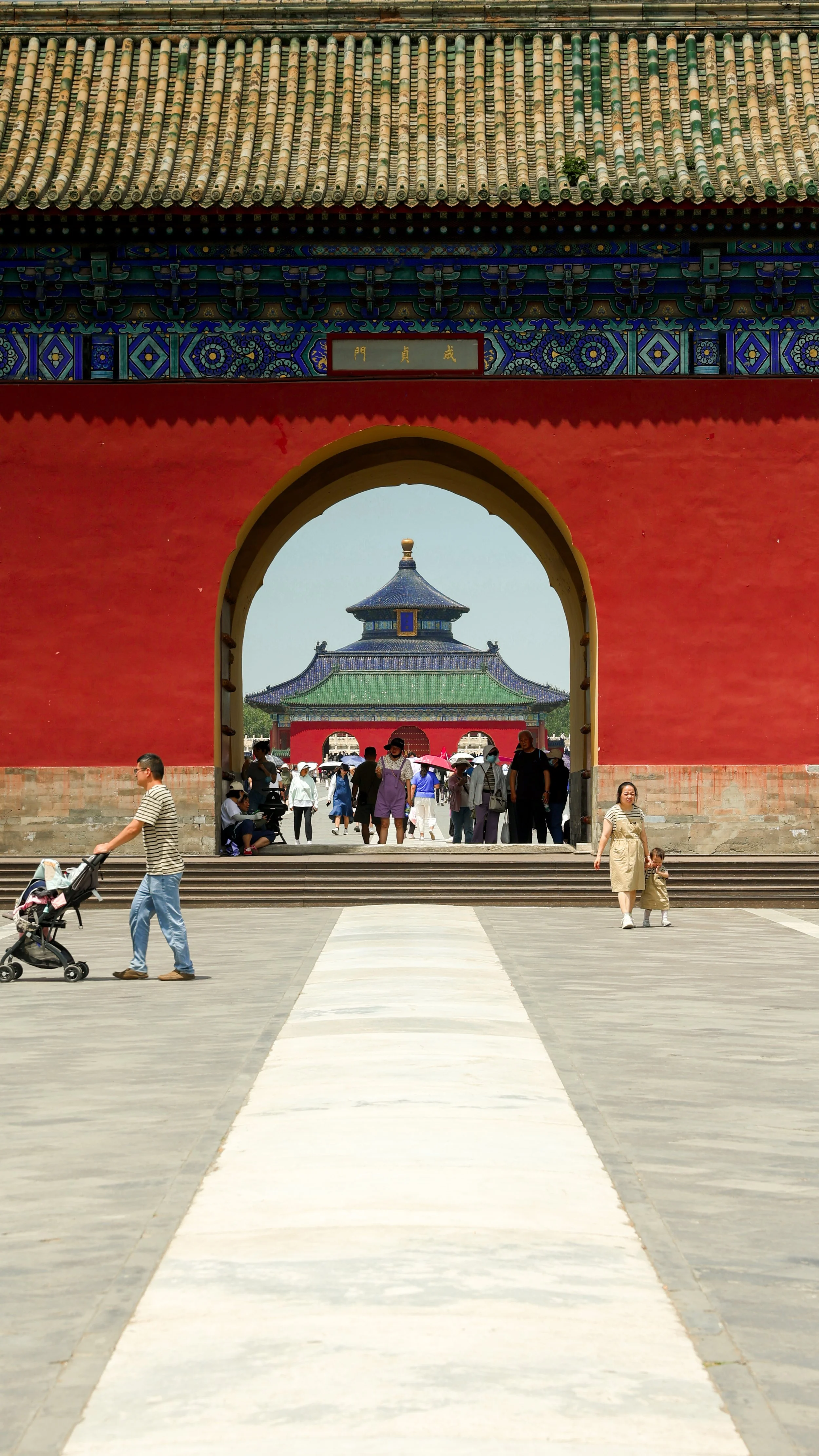 Photograph of Temple of Heaven in Beijing, with people walking through, leading to a building with a blue-tiled roof in the distance.