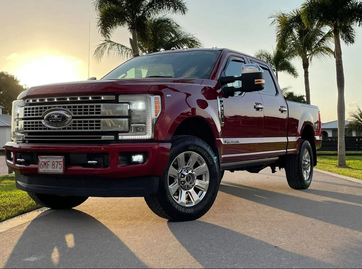 Red Ford F-250 Super Duty pickup truck parked on a driveway with palm trees in the background during sunset.