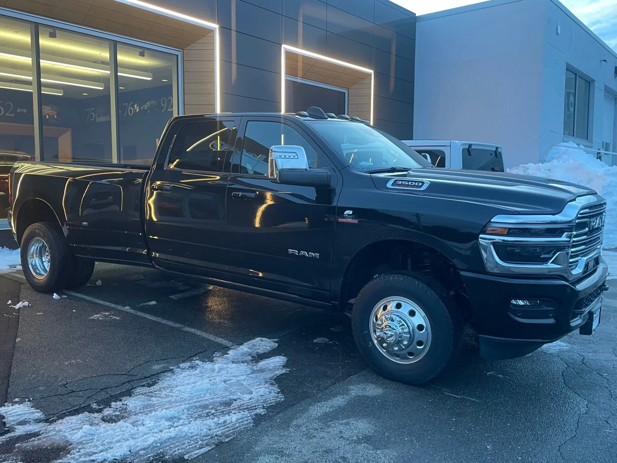 A black RAM pickup truck parked outside a dealership with a modern exterior, snow on the ground, and a clear sky.