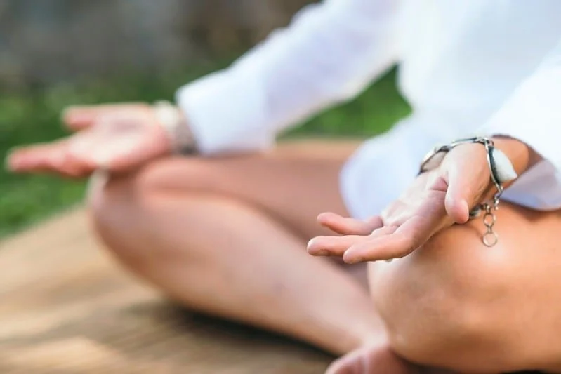 Person practicing meditation outdoors, seated cross-legged on a mat, with hands in a mudra position.