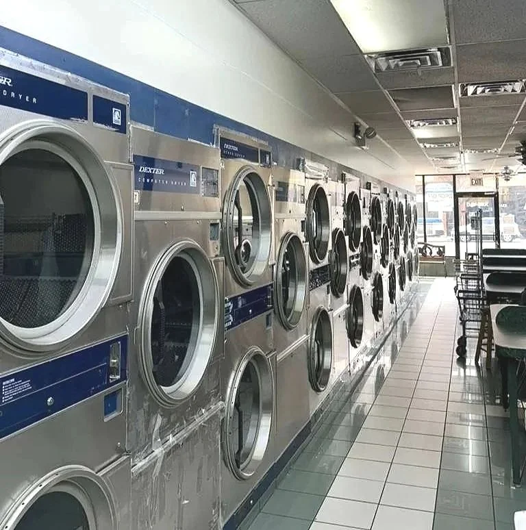 A row of washing machines in a laundromat, with chairs and tables near the front window.