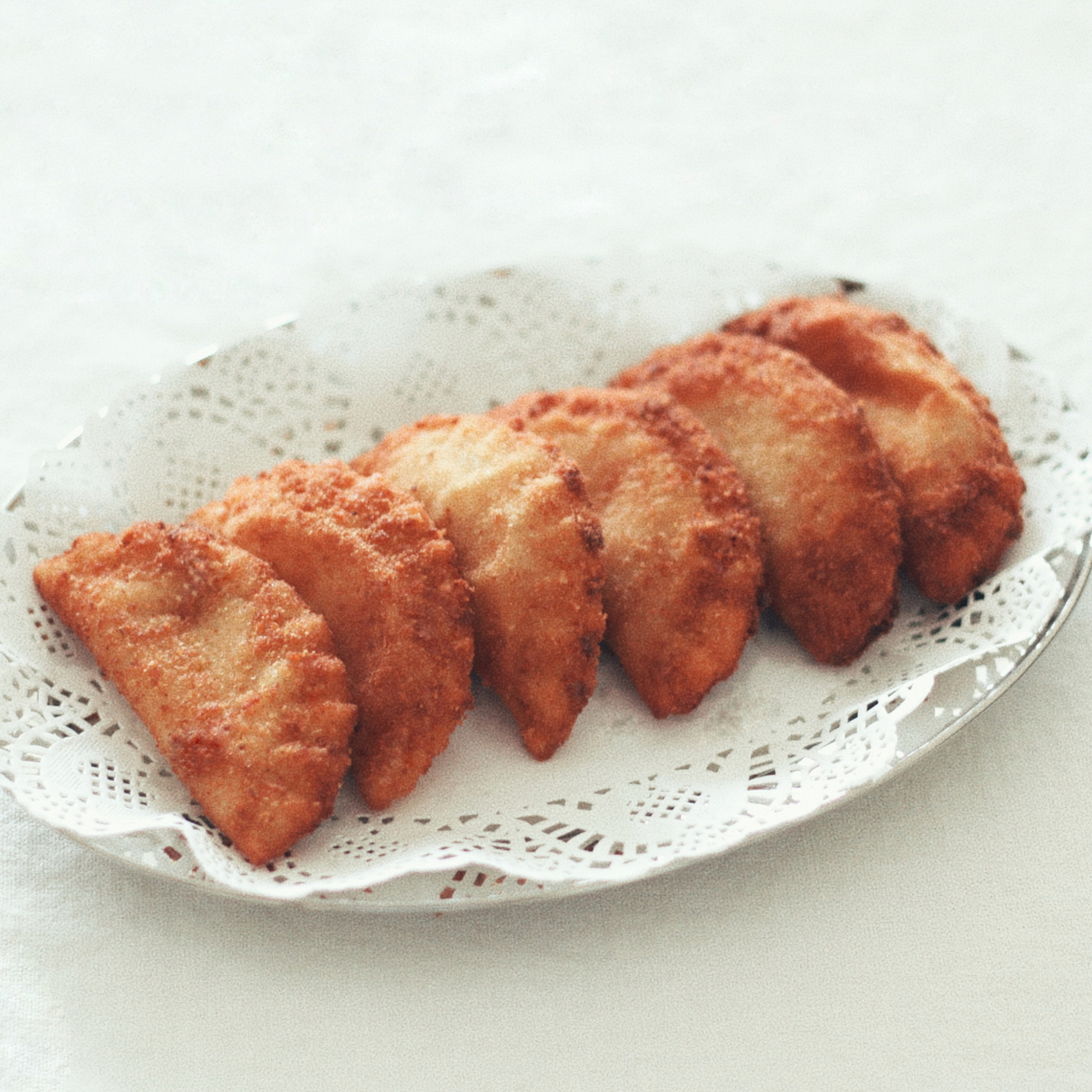 A selection of golden, handmade Portuguese rissois arranged on a white serving platter, available with shrimp and chouriço/sausage fillings.