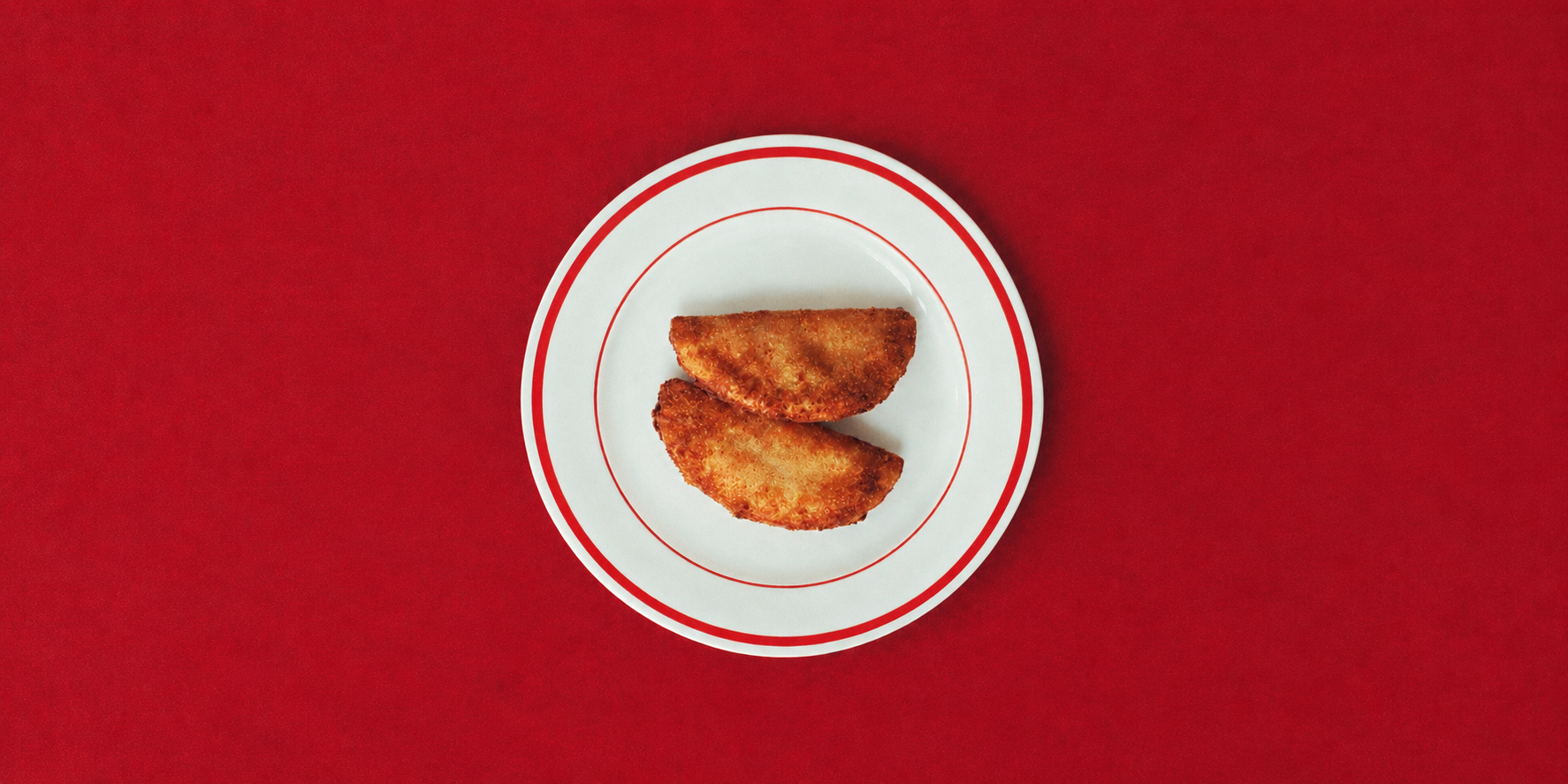 Two golden, crispy handmade Portuguese rissois on a white plate with red trim, photographed against a vibrant red background.