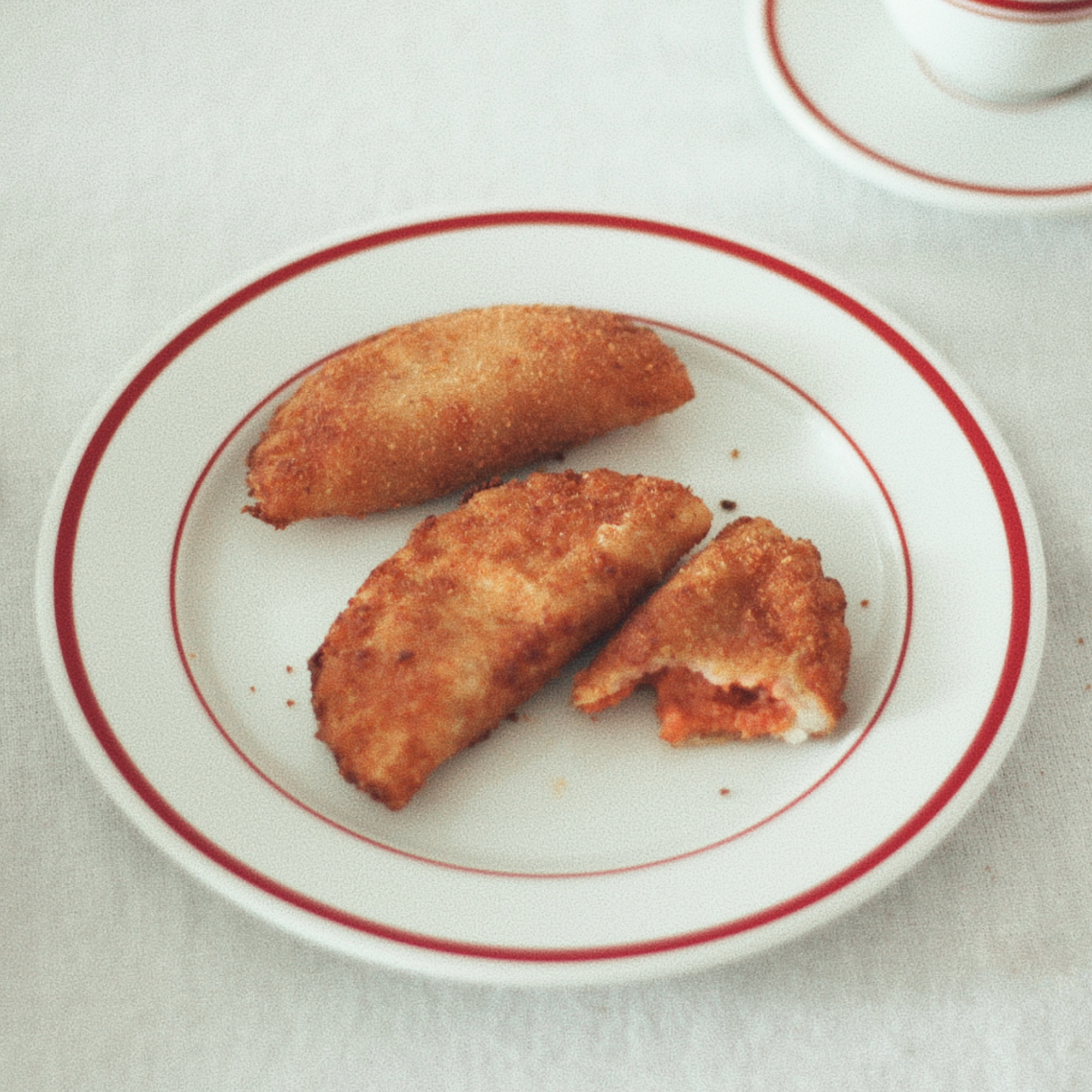 Golden, crispy Portuguese chouriço/sausage rissois on a white plate, with one patty cut open to show its smoked sausage filling.
