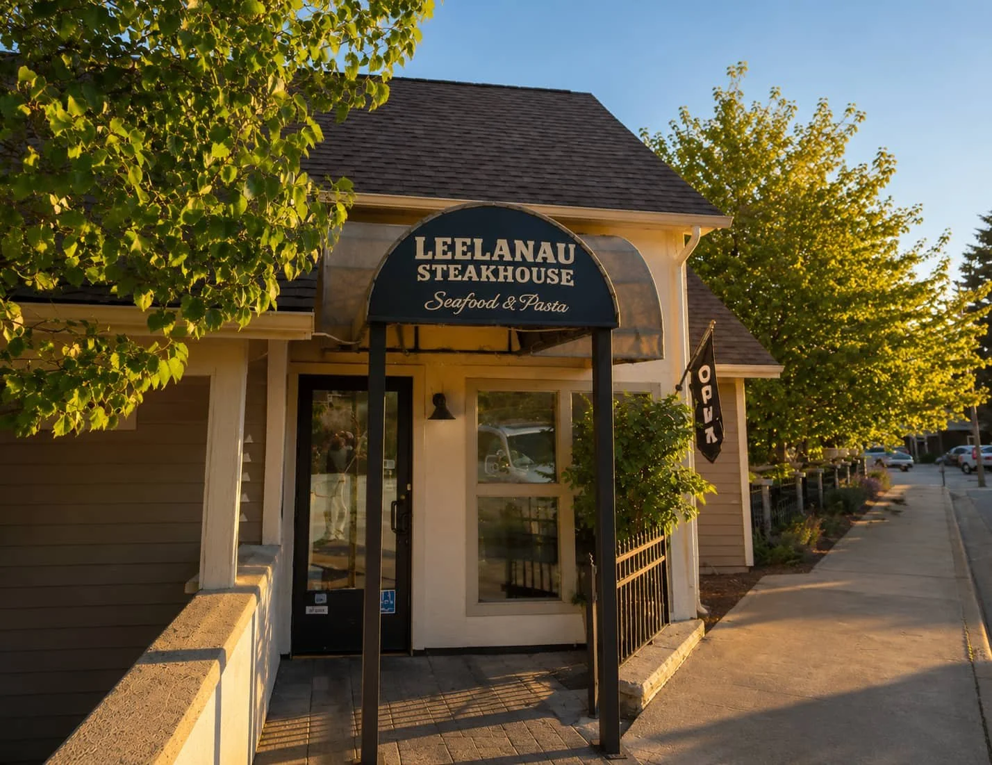 Exterior entrance to Leelanau Steakhouse Seafood & Pasta with dark awning signage, landscaping, and welcoming storefront at 104 Main St in Lake Leelanau